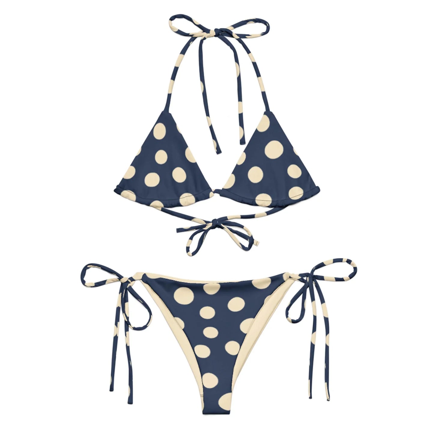 A navy blue Mambí bikini with large cream-colored polka dots. The top features a triangle style with halter and back ties, while the bottoms have adjustable side ties.