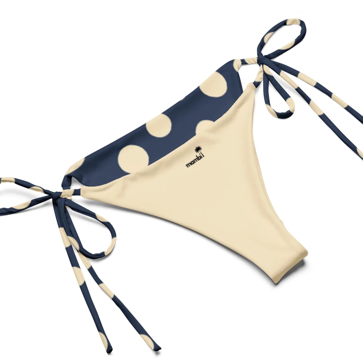 Beige bikini bottom with navy blue waistband and side ties, decorated with large cream polka dots. The brand name monini and a subtle Mambí accent appear near the waistband.