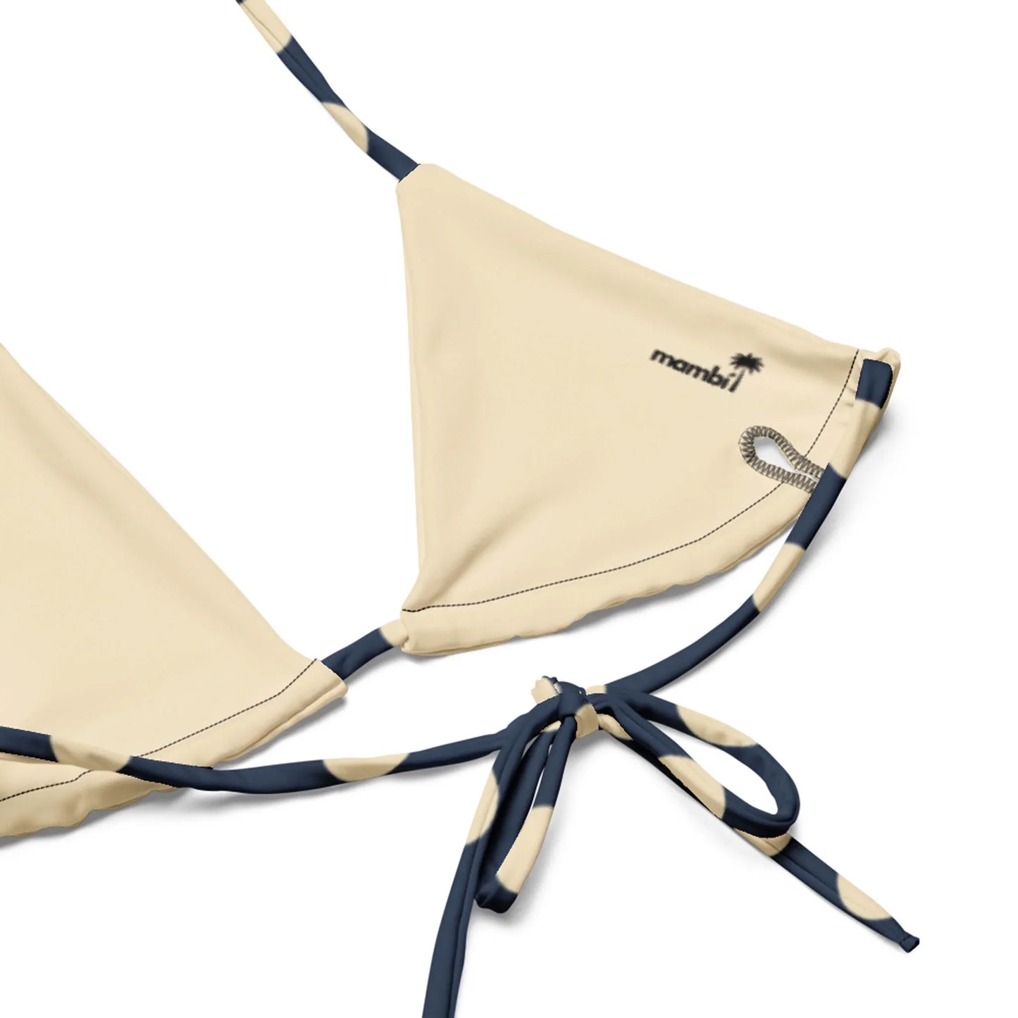 Close-up of a beige bikini top with navy blue straps, featuring a small palm tree graphic and the word Mambí printed near the top edge.