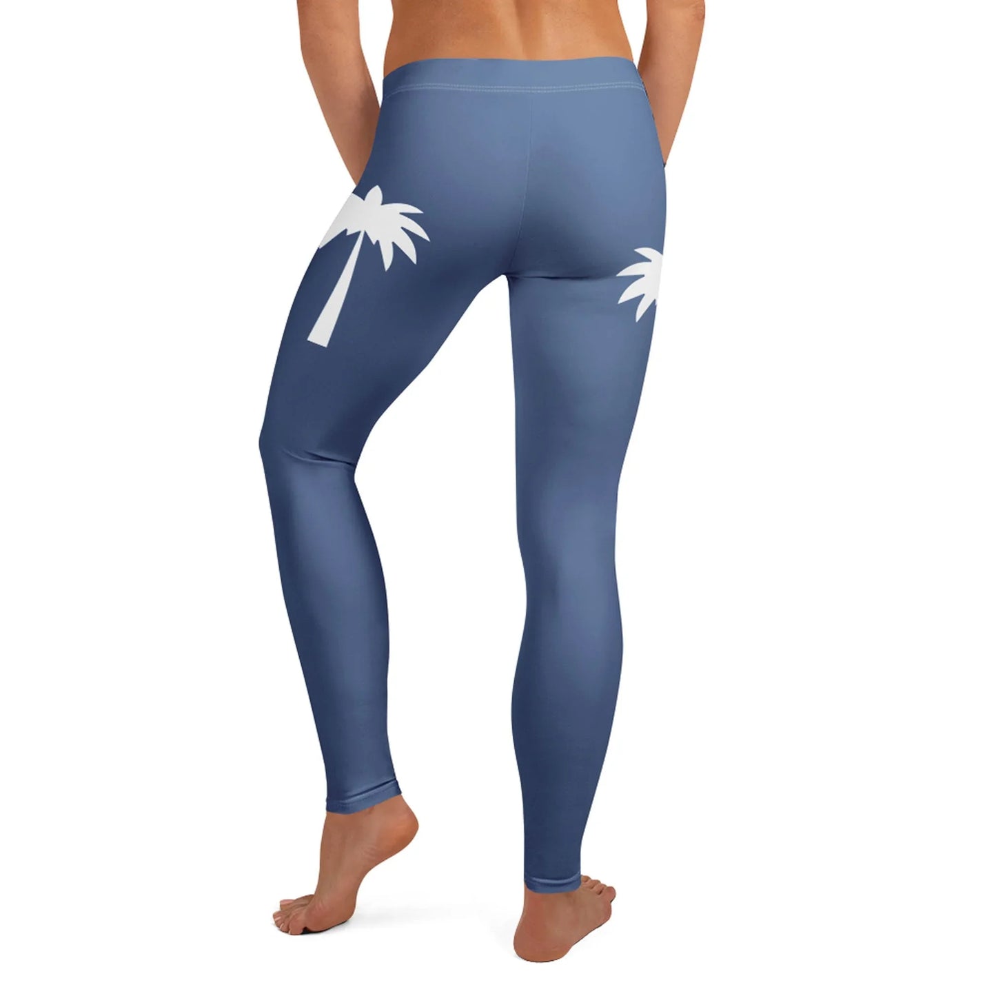 A person wearing high-waisted blue Mambí leggings with white palm tree graphics on the back, standing barefoot and facing away from the camera.
