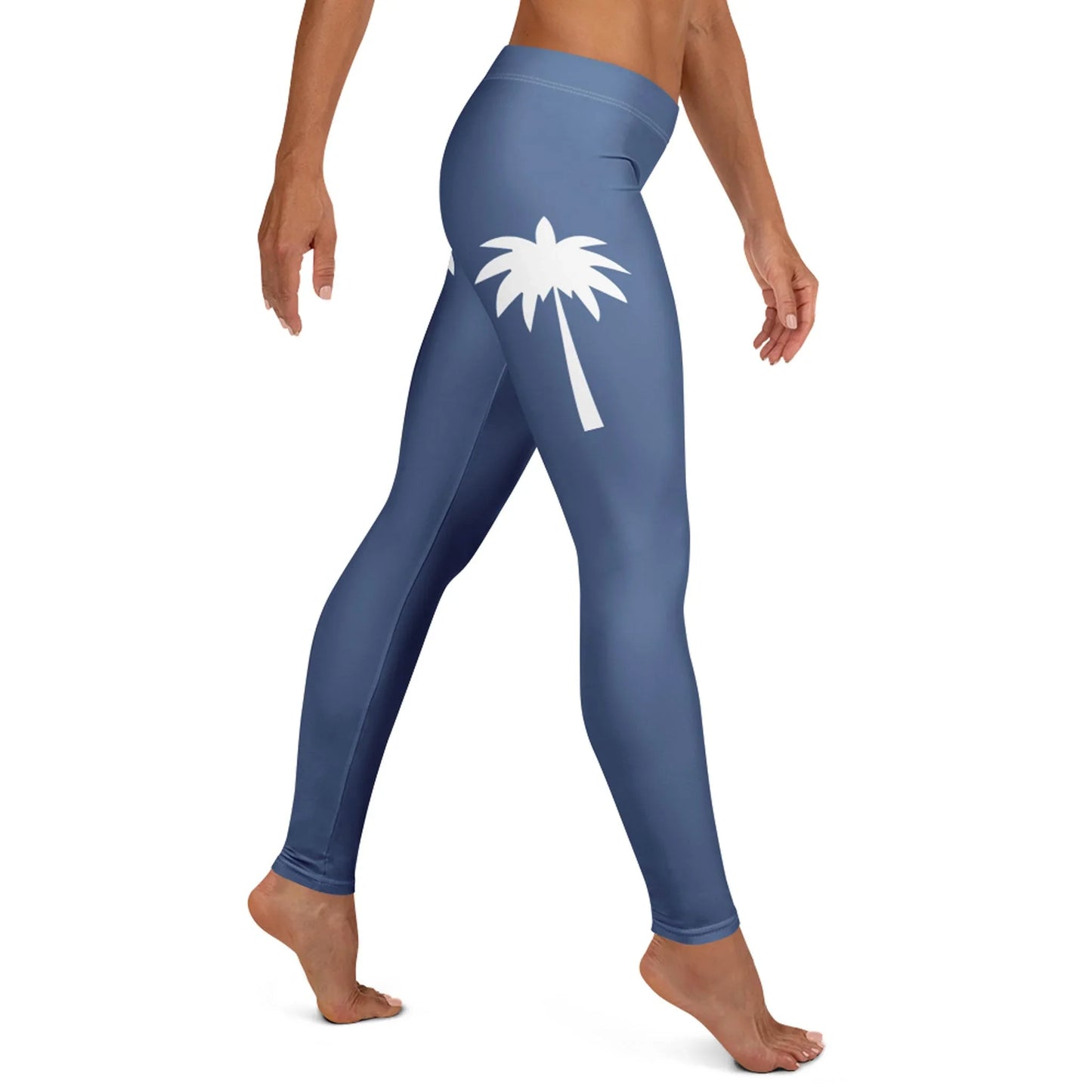 A person wearing high-waisted, blue Mambí leggings with a white palm tree graphic on the upper thigh, standing barefoot and viewed from the side.