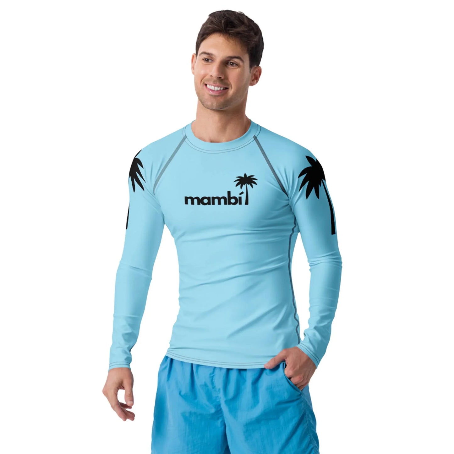 A man wearing a light blue long-sleeve rash guard with black palm tree graphics on the shoulders and Mambí on the chest, paired with matching swim shorts. He is smiling and standing with one hand in his pocket.