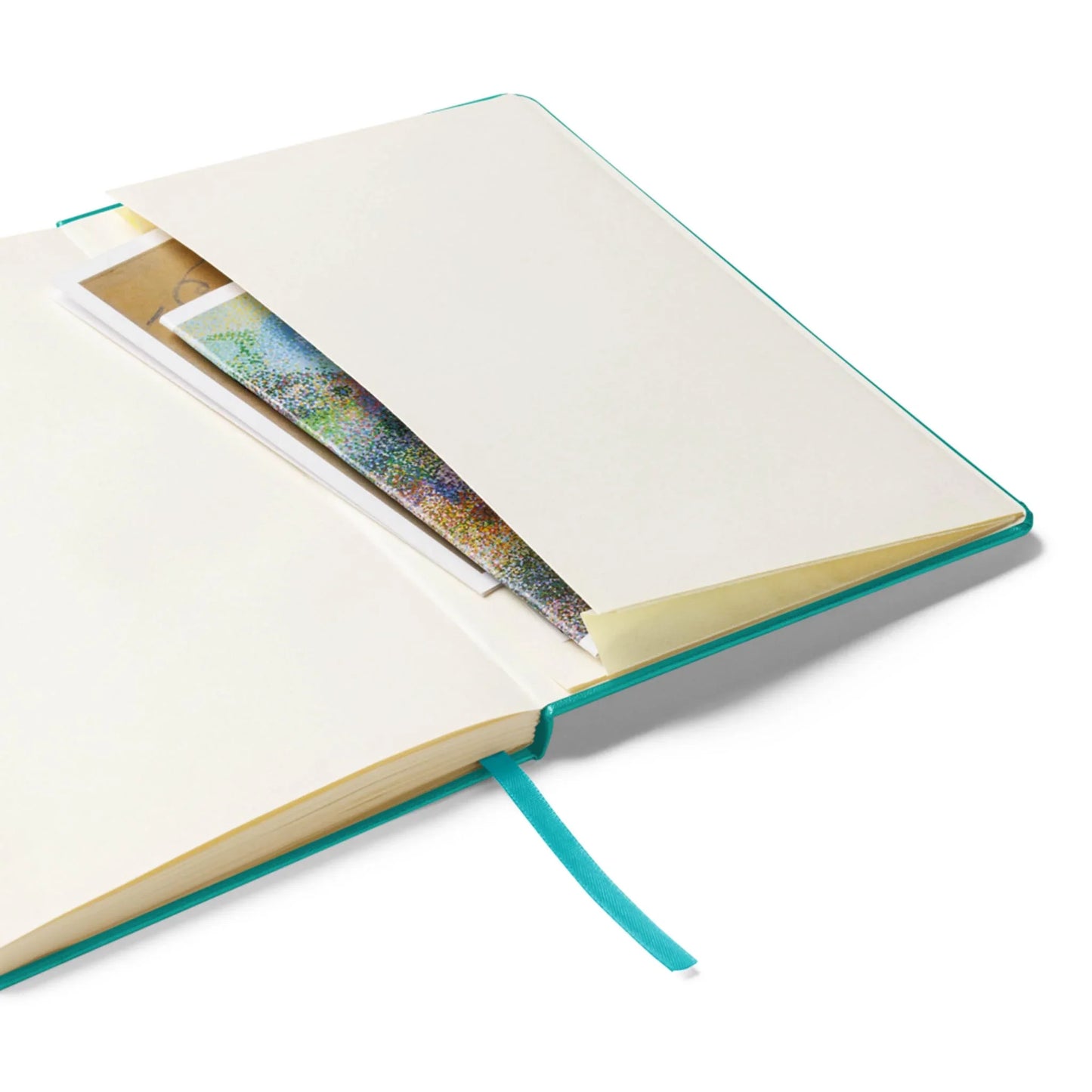 An open Mambí notebook with a teal cover and ribbon bookmark, featuring an inside pocket at the back that holds colorful papers and envelopes.