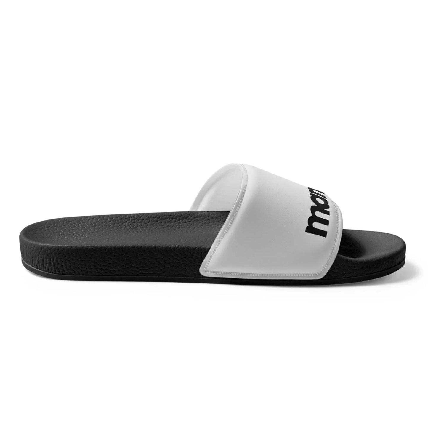 A black Mambí slide sandal with a textured sole and a white strap across the top, featuring black text. The sandal is shown from a side view on a plain white background.