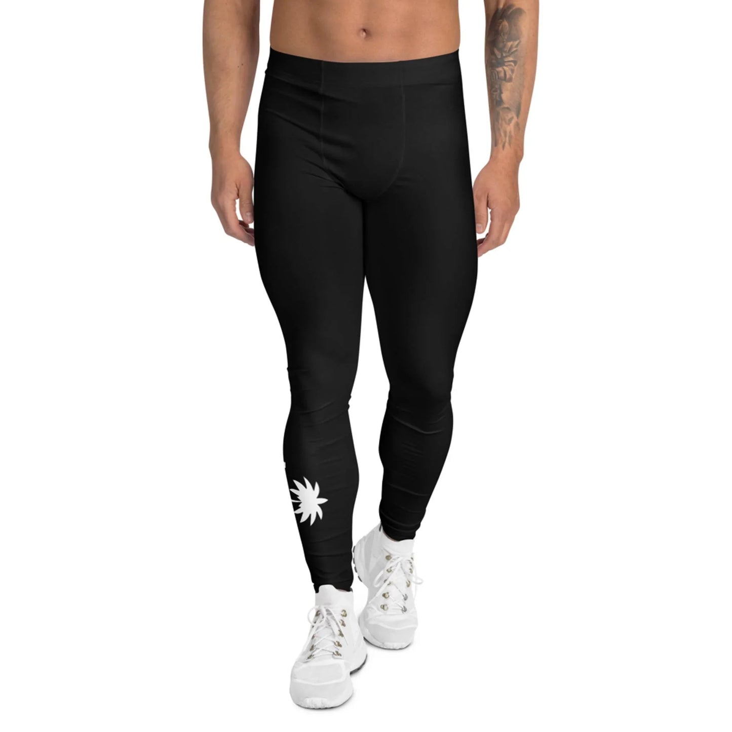 A person wearing Mambí black leggings with a white sunburst design near the left ankle, paired with white sneakers, stands against a plain white background.
