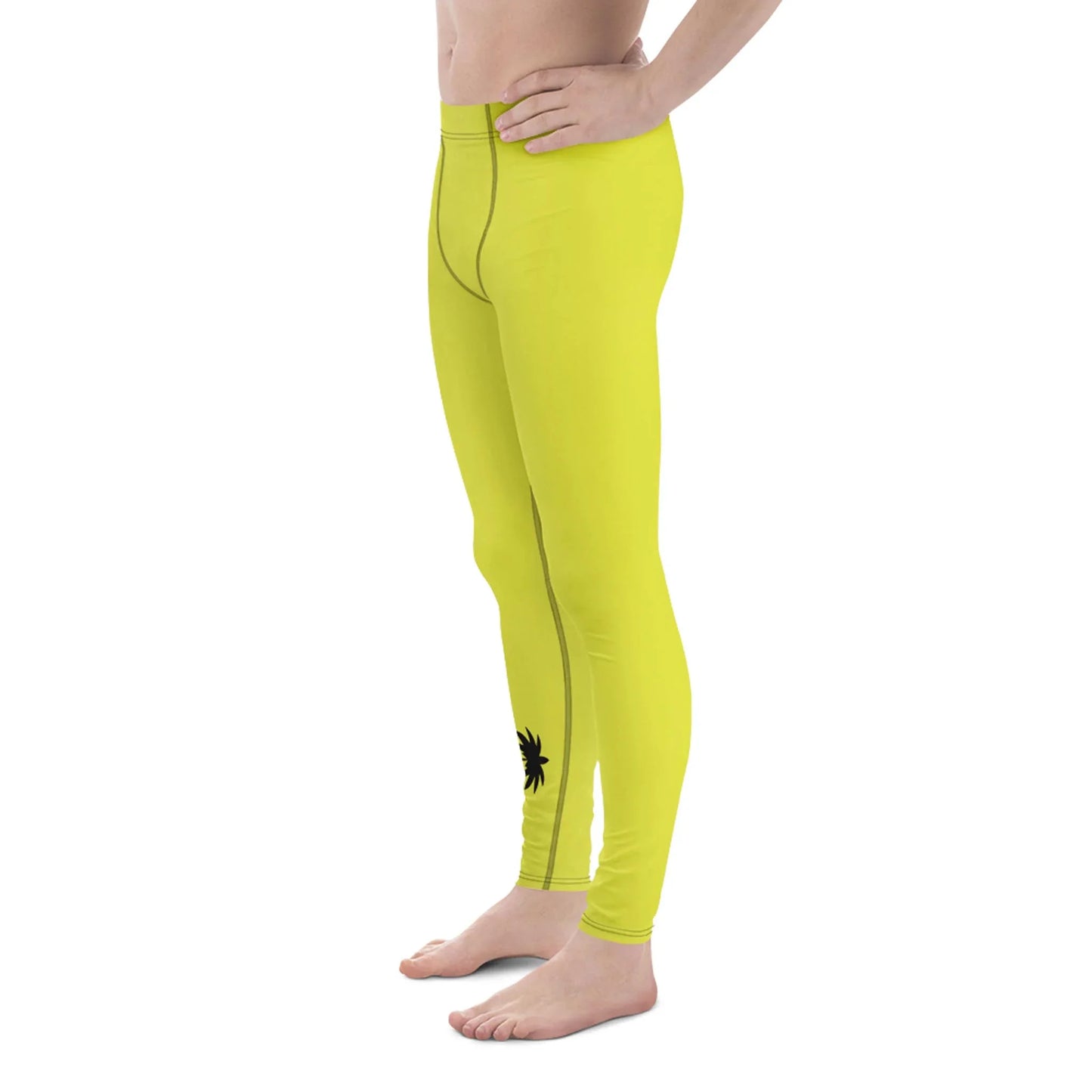 A person stands barefoot in bright yellow Mambí leggings with a small black design near the left ankle, shown from the side with hands resting by the waist. The upper body is not fully visible.