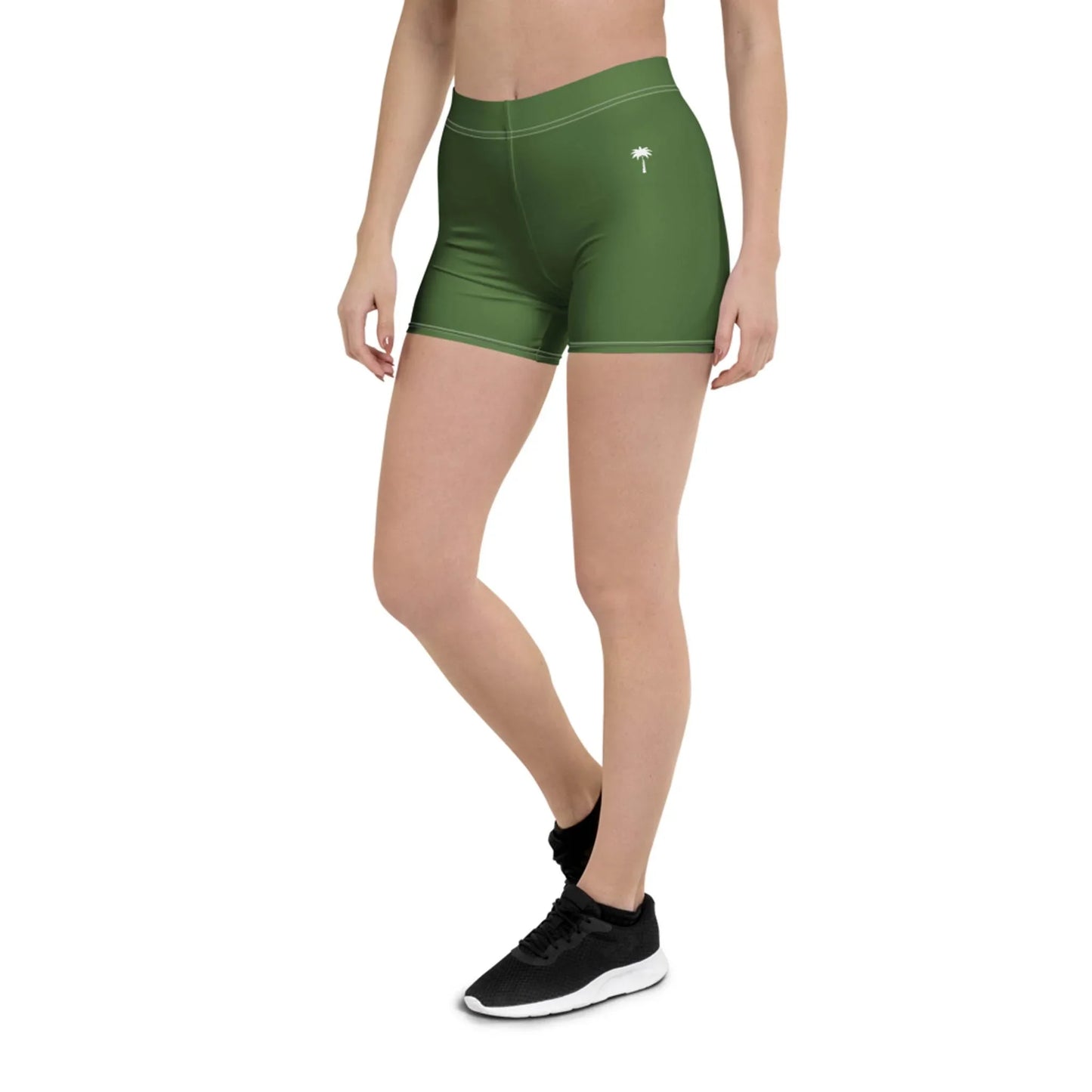 A person wearing green Mambí athletic shorts and black sneakers stands with one leg slightly bent. Only the lower torso and legs are visible. The shorts feature a small white palm tree graphic on the left thigh.