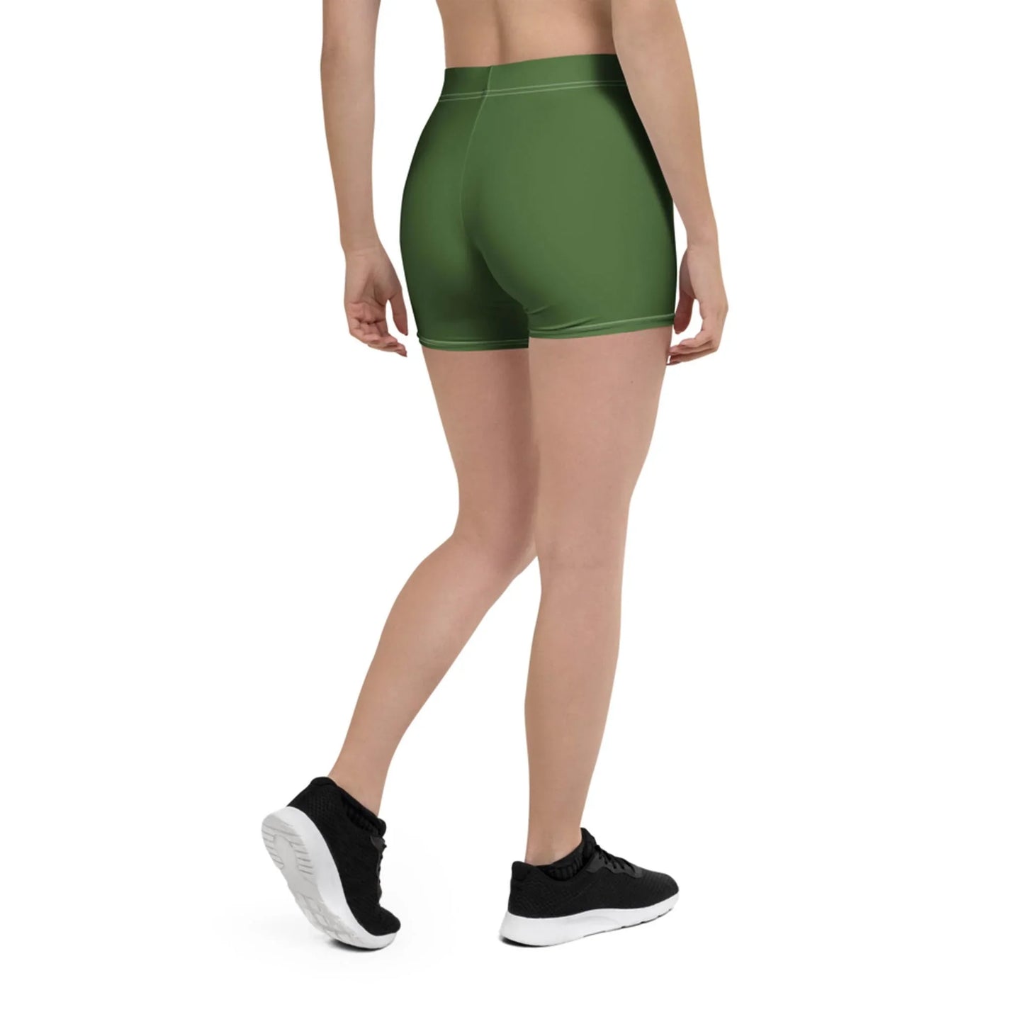 A person stands facing away, wearing green high-waisted Mambí athletic shorts, a beige top, and black sneakers against a plain white background.