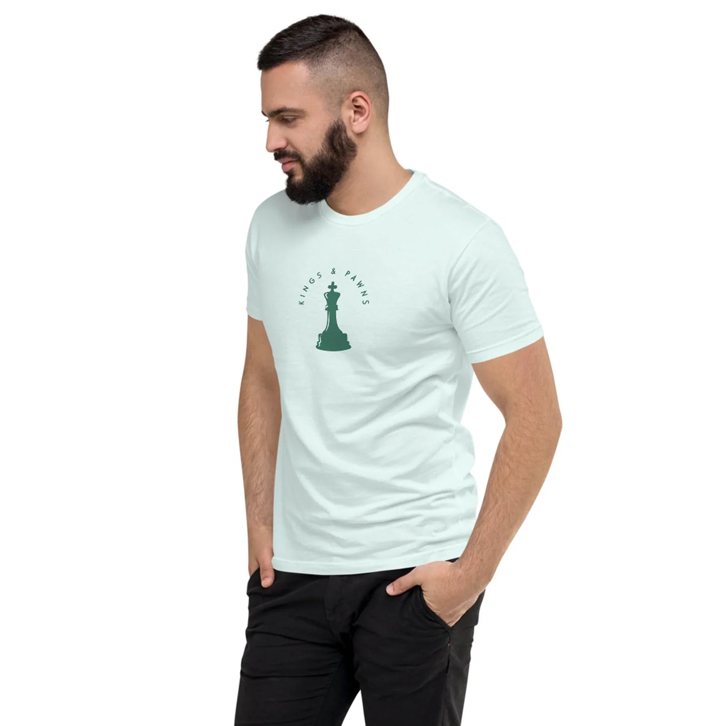 A man with a beard stands, looking to his left, wearing a light-colored Mambí t-shirt with a small chess piece graphic and the words Kings & Pawns on the chest. His hands are in his pockets.