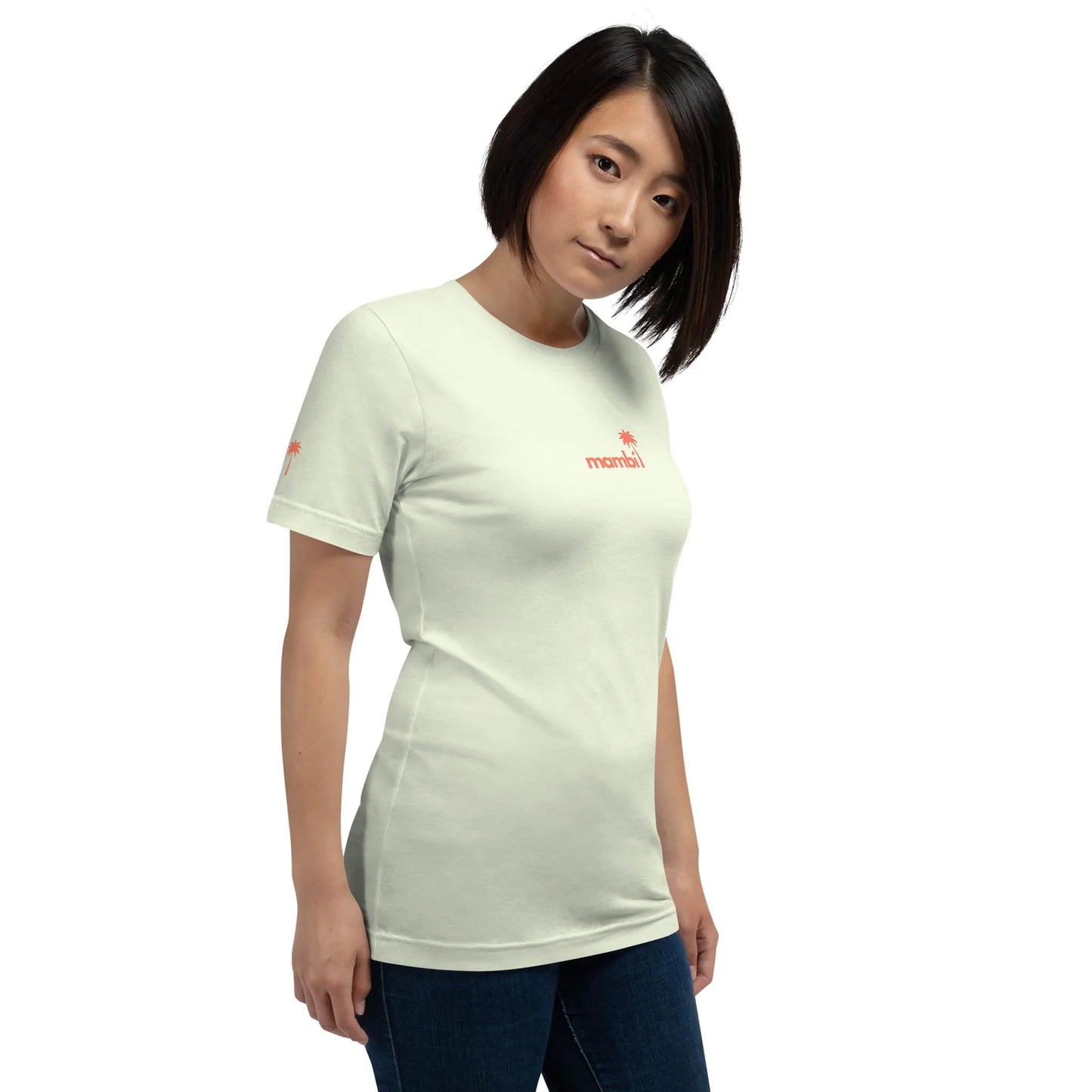 A woman with straight black hair wears the Printful Knowledge Graphic Tee, a comfy unisex cotton shirt featuring bold red mamba text on the chest, paired with dark jeans. She stands against a plain white background.