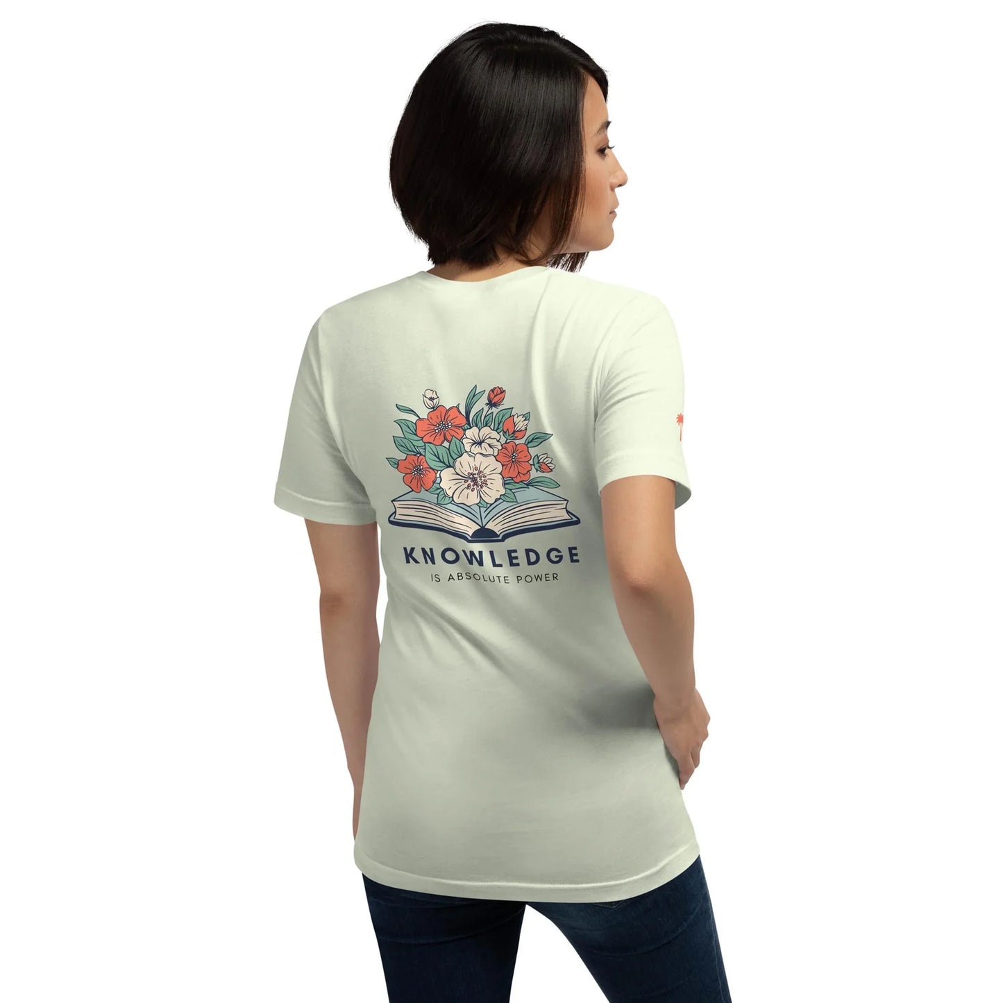 A woman faces away from the camera, wearing the Printful Knowledge Graphic Tee—a comfy unisex cotton shirt with a floral design sprouting from an open book and “KNOWLEDGE IS ABSOLUTE POWER” below.