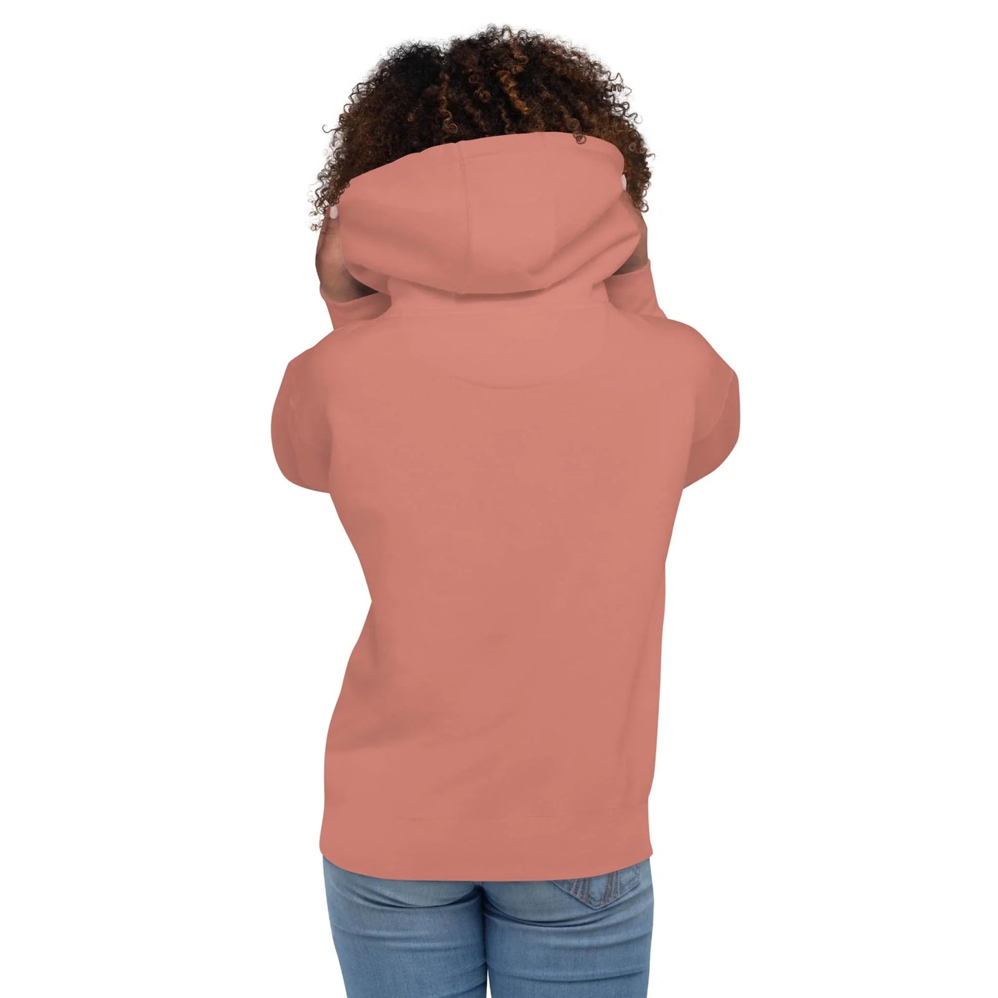 A person with curly hair, seen from behind, wears a rose-colored Mambí hoodie and blue jeans. The hood is up, partially covering their head and shoulders.