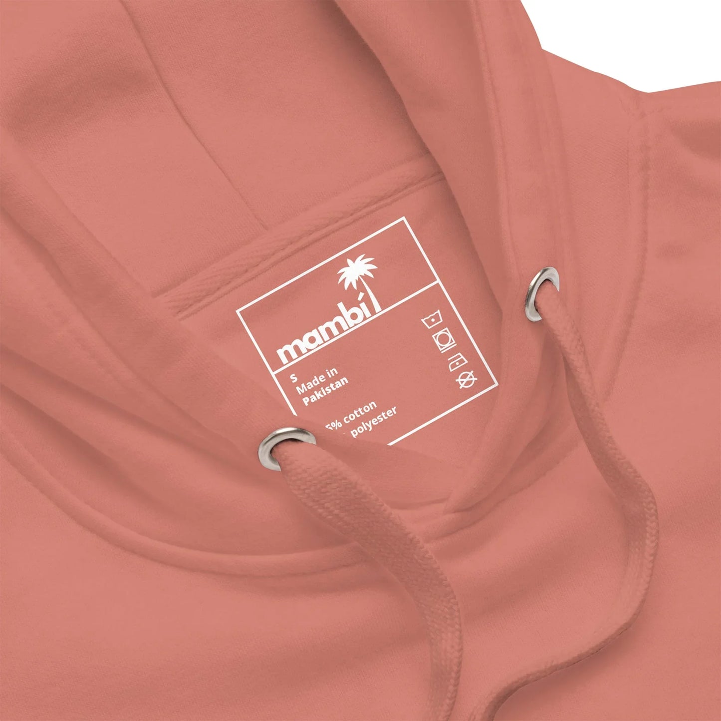 A close-up of a salmon-colored hoodie with a visible inner neck label showing the Mambí brand, size S, made in Pakistan, and fabric details: 84% cotton, 16% polyester. The label features laundry symbols and a palm tree icon.