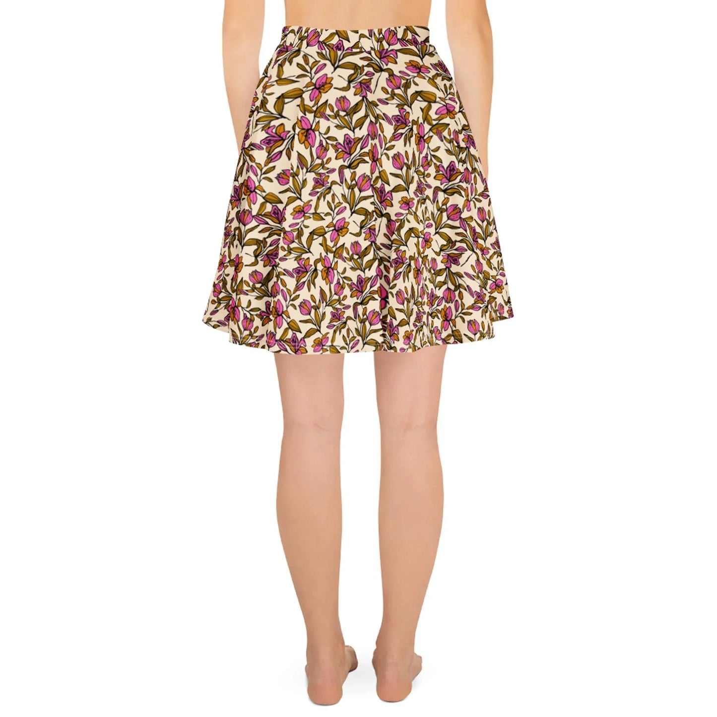 A woman standing barefoot, shown from the back, wears a Mambí knee-length skirt with a colorful floral print in shades of pink, green, and yellow on a cream background.