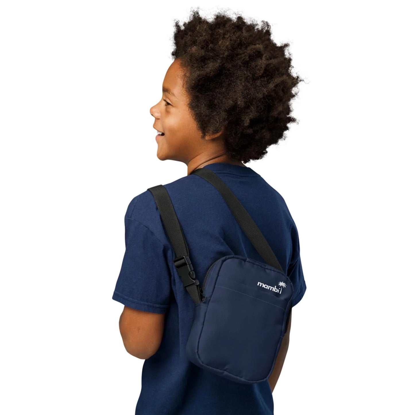 A smiling child with curly hair wearing a navy blue t-shirt and carrying a small Mambí navy crossbody bag on their shoulder, viewed from the back and side against a white background.
