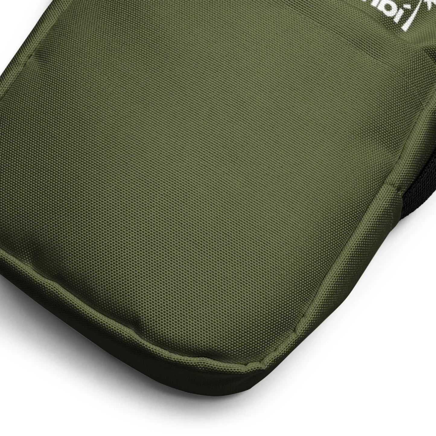 Close-up view of the bottom corner of an olive green Mambí fabric backpack, showing its textured material and reinforced stitching. Part of a white logo is visible at the top edge of the image.
