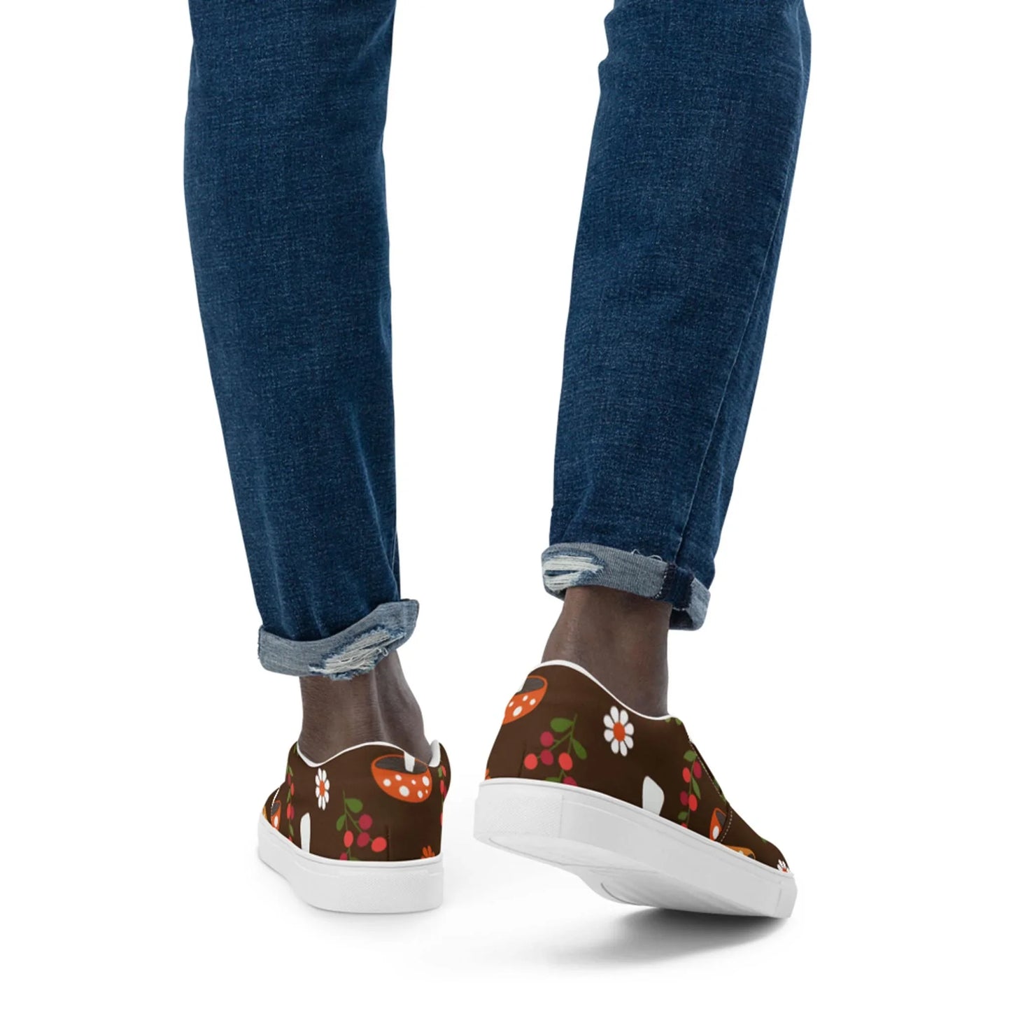 A person stands against a white background, wearing rolled-up blue jeans and Printfuls Mario Handmade Slip-On Canvas Shoes for men, featuring a whimsical mushroom and floral pattern—a unique style statement.