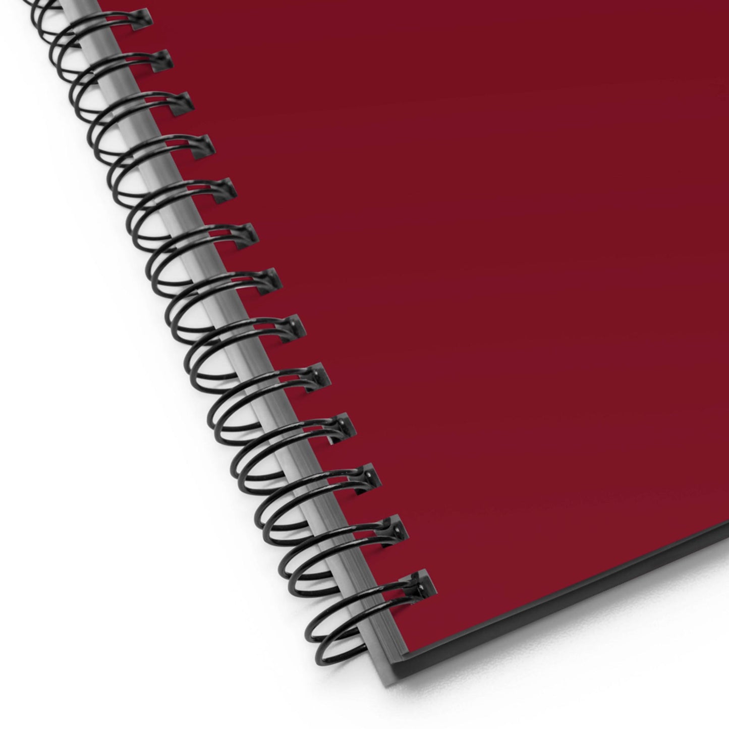 A close-up view of the bottom-right corner of a custom wire-bound notebook with a dark red cover. The black metal spiral binding is clearly visible along the notebook’s edge.