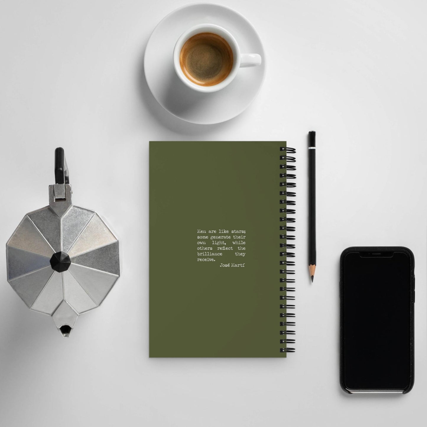 Flat lay of a coffee cup, silver moka pot, daily companion notebook with text, black pencil, and smartphone on a white surface.