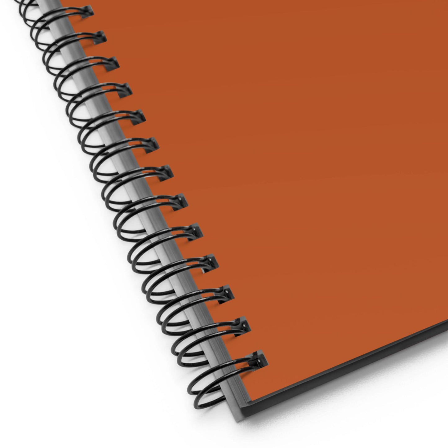 Close-up of a spiral notebook with an orange cover, viewed at an angle from the corner, showing the black metal spiral binding and part of the cover on a white background.