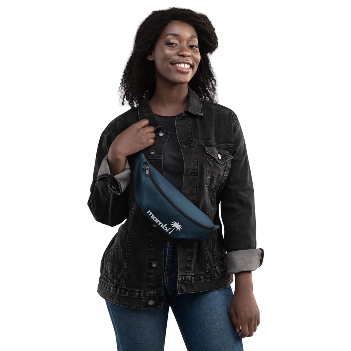 Smiling woman with curly hair wears a black denim jacket and blue jeans, holding a navy blue crossbody bag featuring the Mambí and a palm tree logo, standing against a white background.
