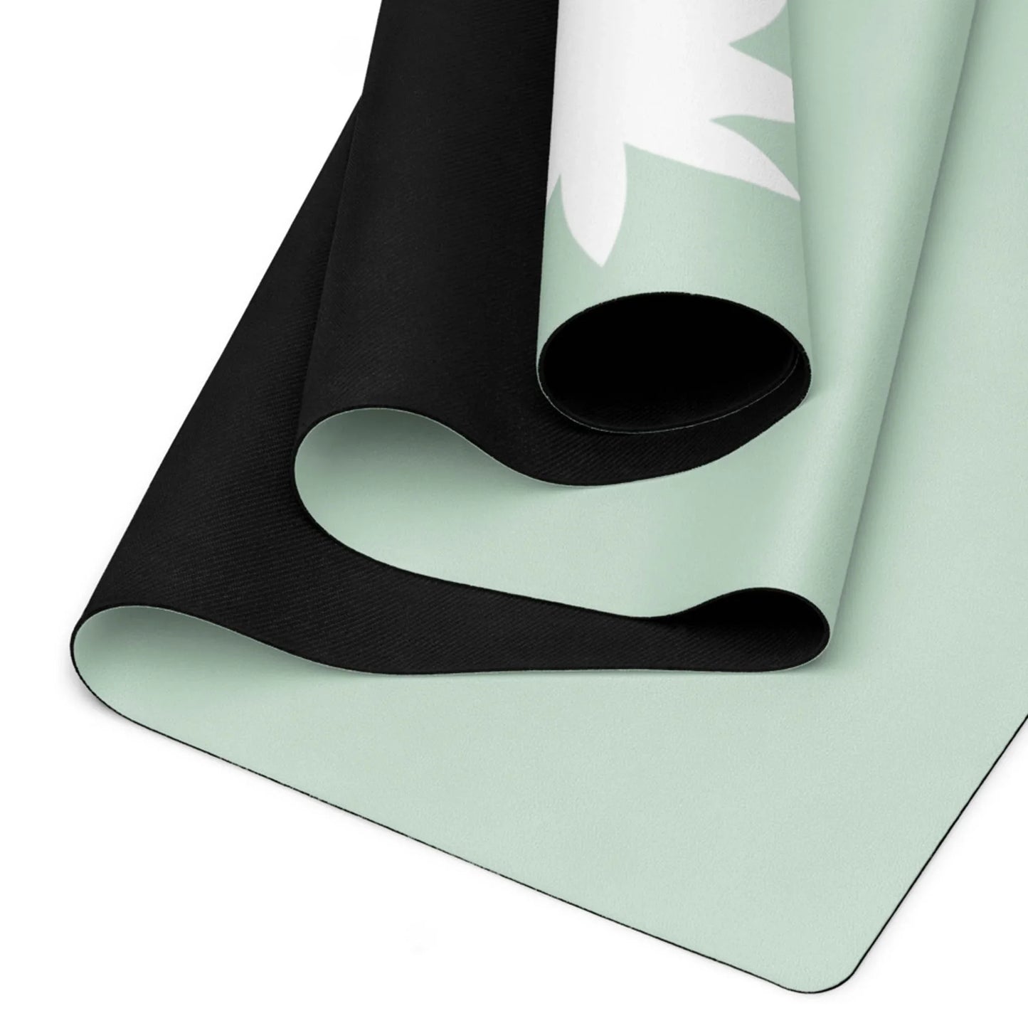 A close-up of two partially rolled Mambí yoga mats. The mats are black on one side and light green on the other, featuring a white leaf design on the green surface.