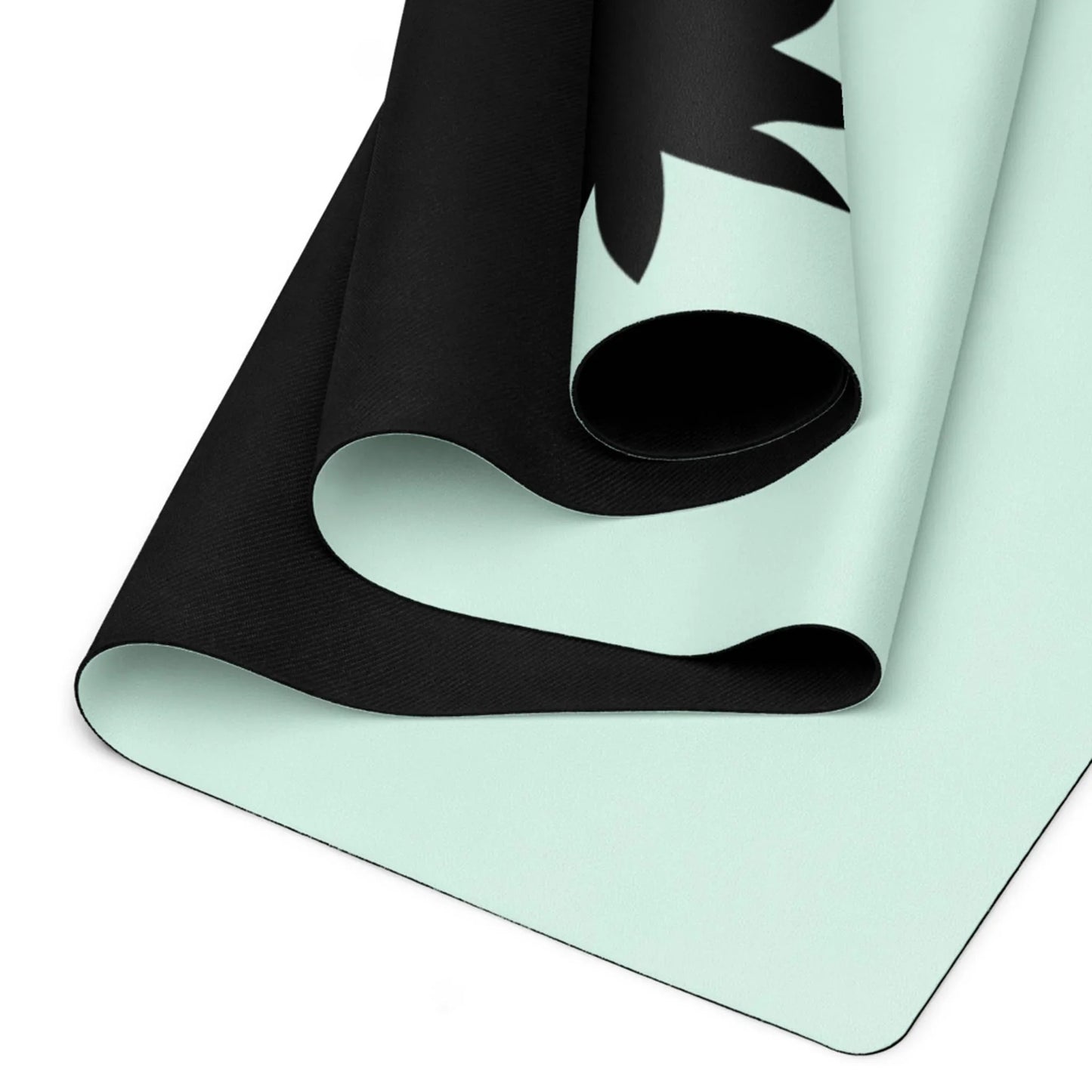 A close-up view of a rolled, light blue Mambí yoga mat with a black underside and a partial black design on the top surface. The mat is shown from an angle, highlighting its thickness and texture.