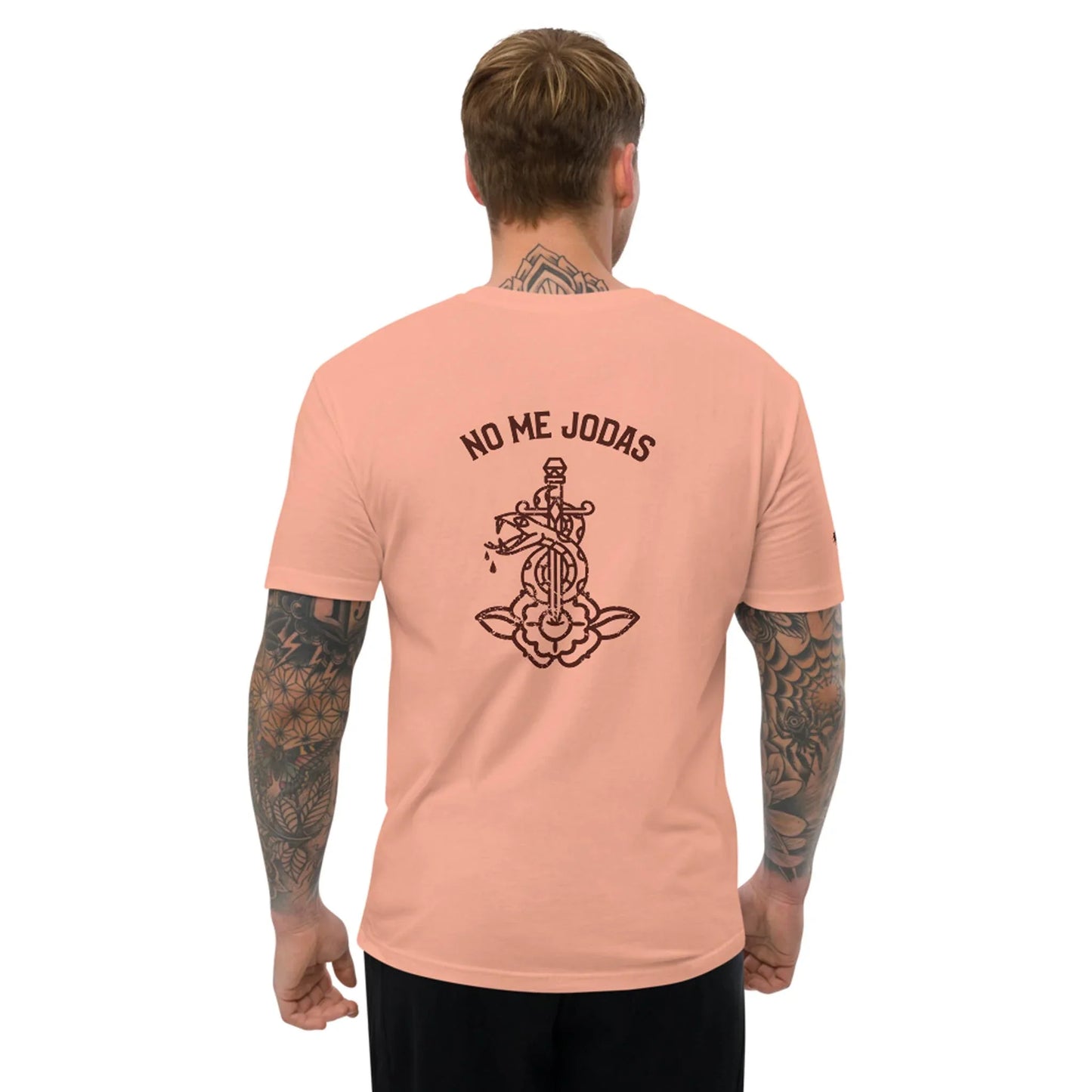 A tattooed man wears the No Me Jodas Fitted Graphic Tee by Printful, a soft cotton mens shirt featuring a sword-pierced heart and flowers graphic with NO ME JODAS text across the back.