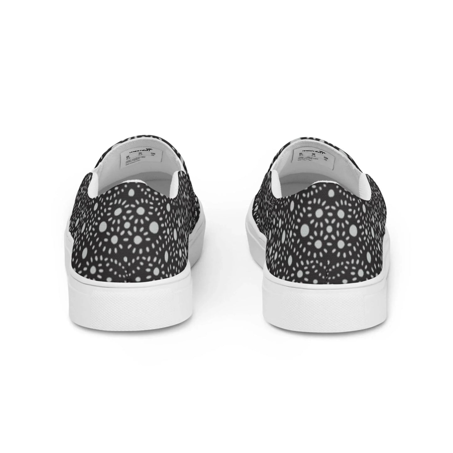 A pair of Mambí slip-on sneakers viewed from the back, featuring a black upper with a white circular geometric pattern and white soles.