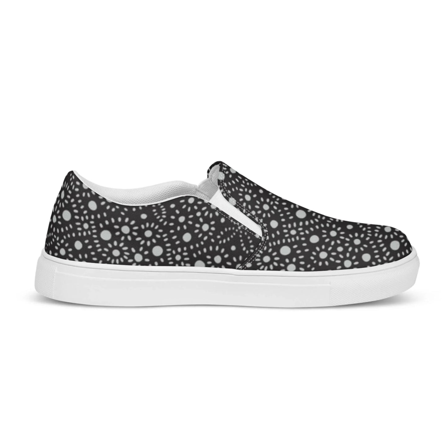 A black slip-on sneaker featuring a white sole and a Mambí-inspired pattern of white circular dots and starburst shapes evenly distributed across the fabric.