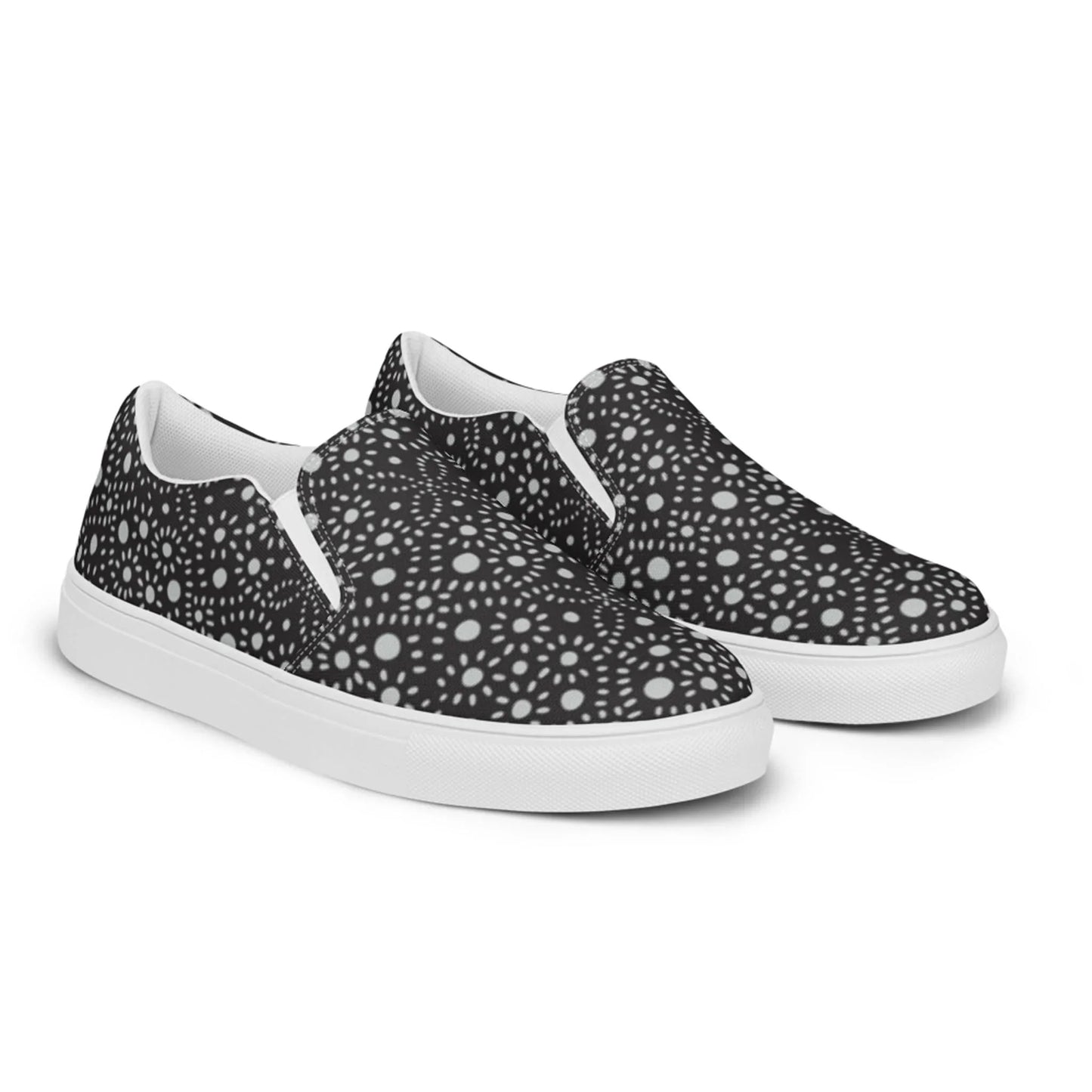 A pair of slip-on sneakers featuring a black background with a white geometric, kaleidoscopic dot pattern. The soles and inner lining are white, giving a modern, stylish Mambí-inspired appearance.