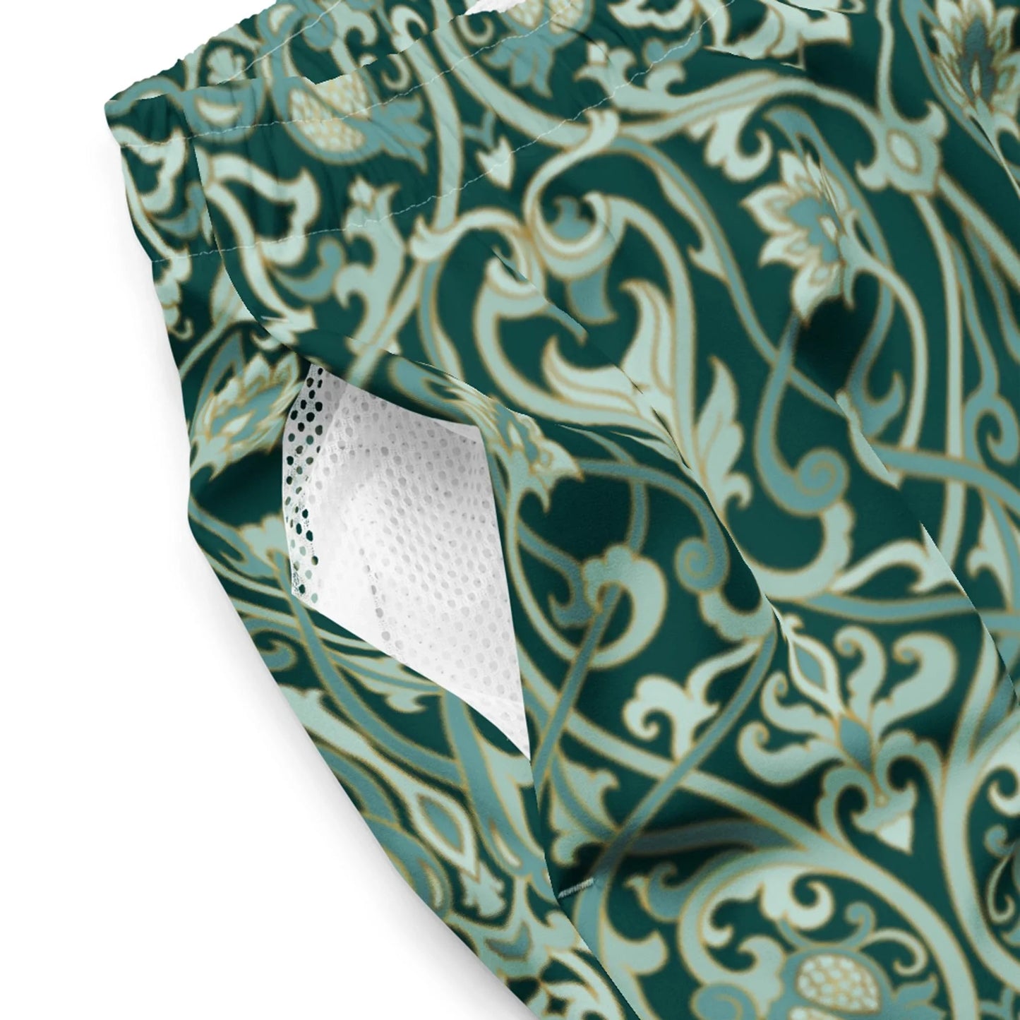Close-up of Printful Oz Swim Trunks for men, featuring a green and beige floral pattern, white mesh-lined pocket, and elastic waistband. Made from water-repellent, four-way stretch fabric for comfort.
