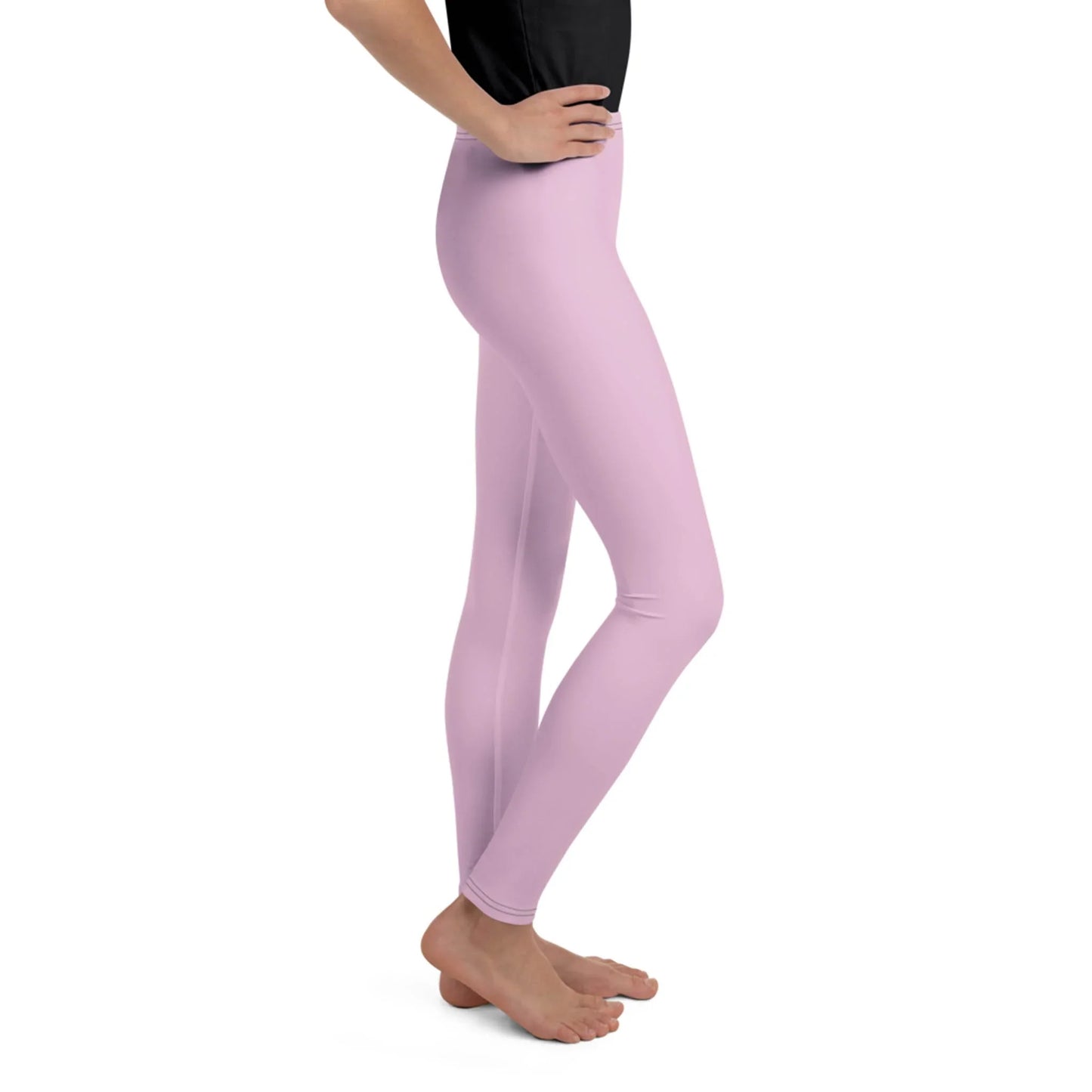 A person stands barefoot in a side pose, wearing light pink Mambí leggings and a black top against a white background. Only the lower half of the body is visible.