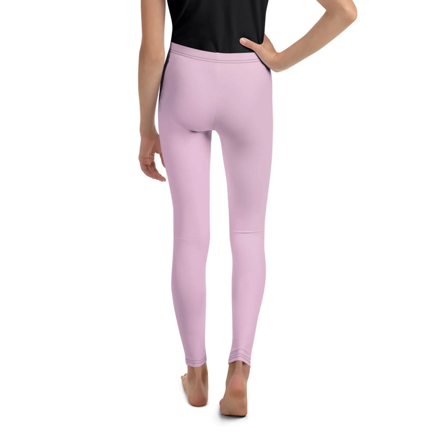 A person stands barefoot on a white background, shown from the back, wearing a black top and light pink Mambí leggings with one hand resting on their hip.