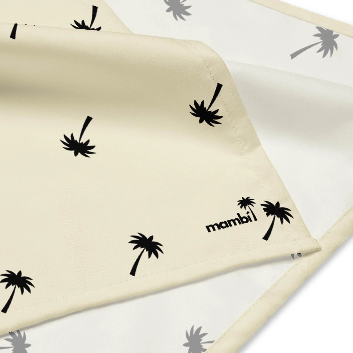 A cream-colored fabric featuring small black palm tree prints and the word Mambí in black text on one corner. The fabric is partially folded, revealing a similar pattern underneath.