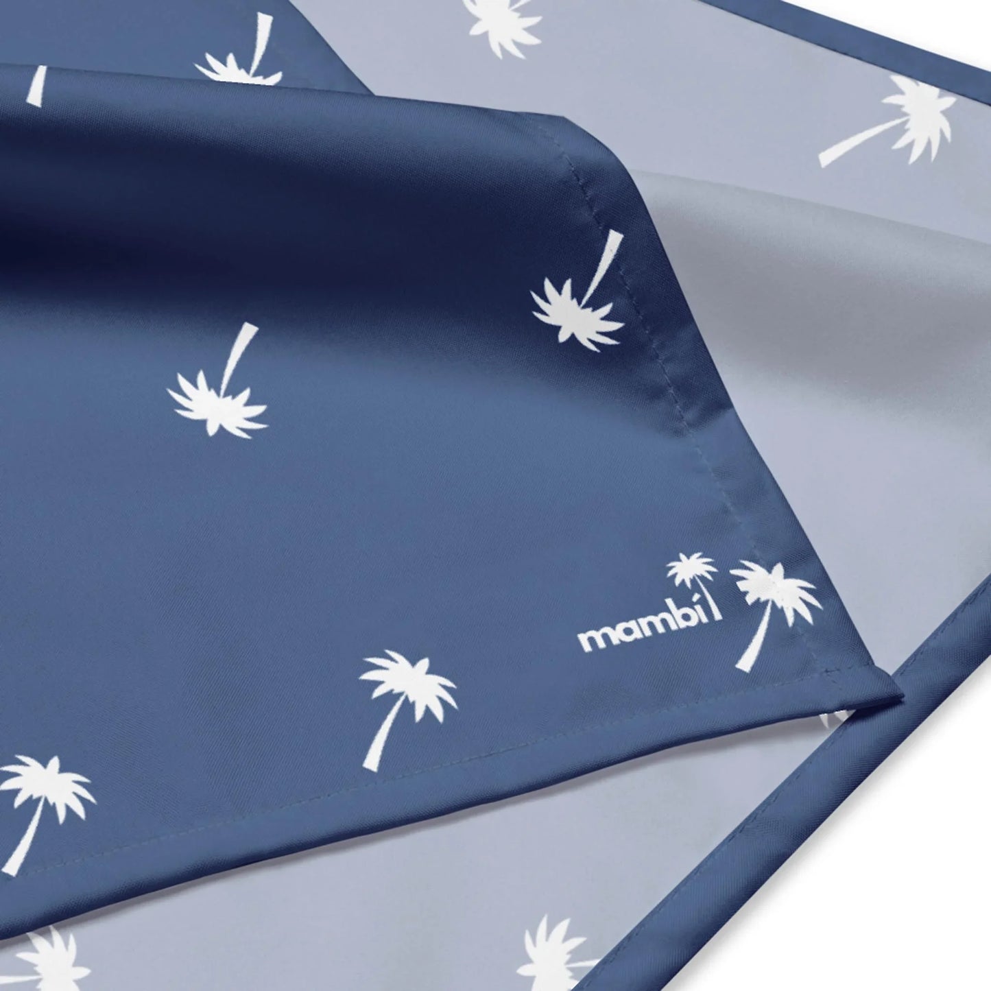 A close-up of a blue and light gray fabric with white palm tree patterns and the word Mambí printed in white near the corner. The fabric appears smooth and soft.
