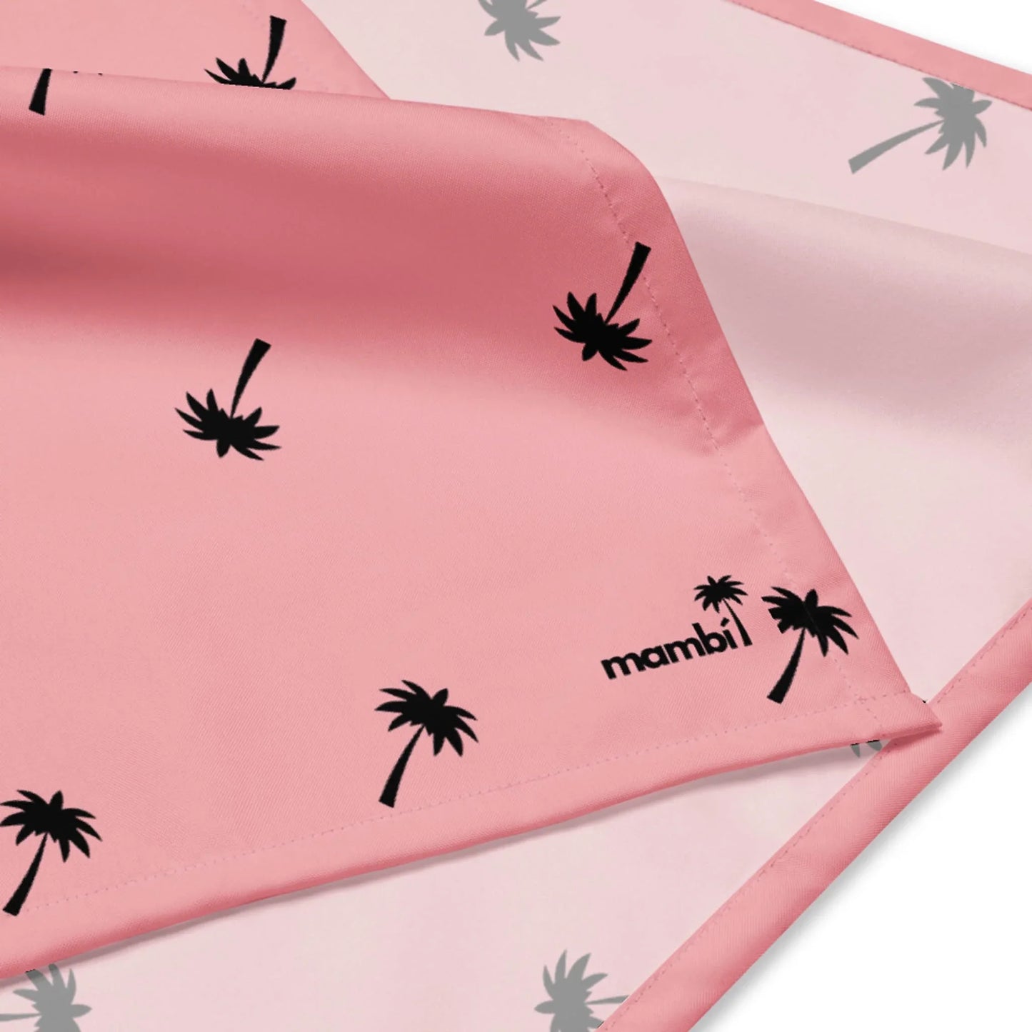 A close-up of pink fabric with black palm tree prints and the word Mambí in black text on the corner. The fabric features neatly stitched edges and a soft, smooth texture.