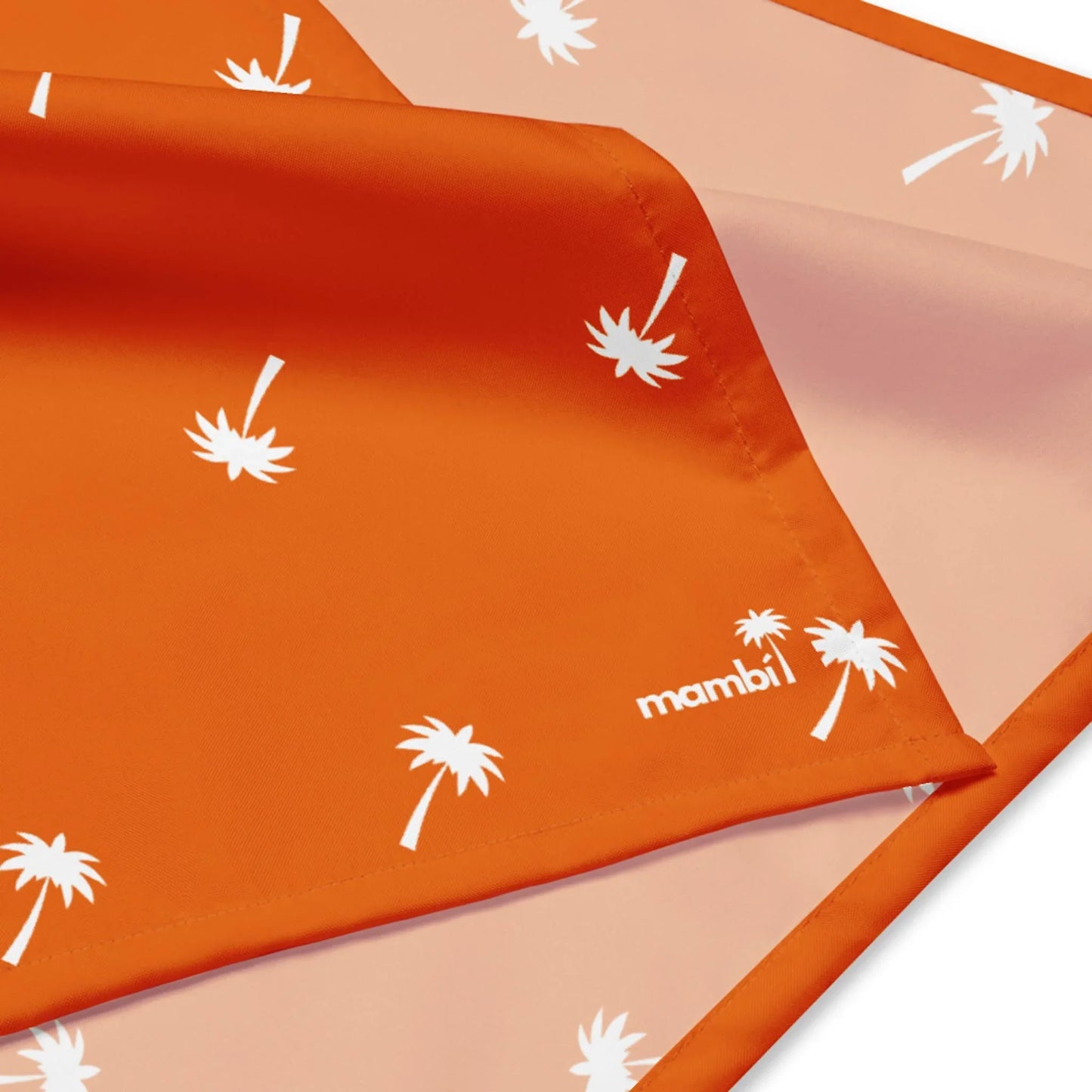 An orange fabric with white palm tree prints and a stitched edge, partially folded to reveal a lighter orange underside with the same pattern and the word Mambí printed in white in the corner.