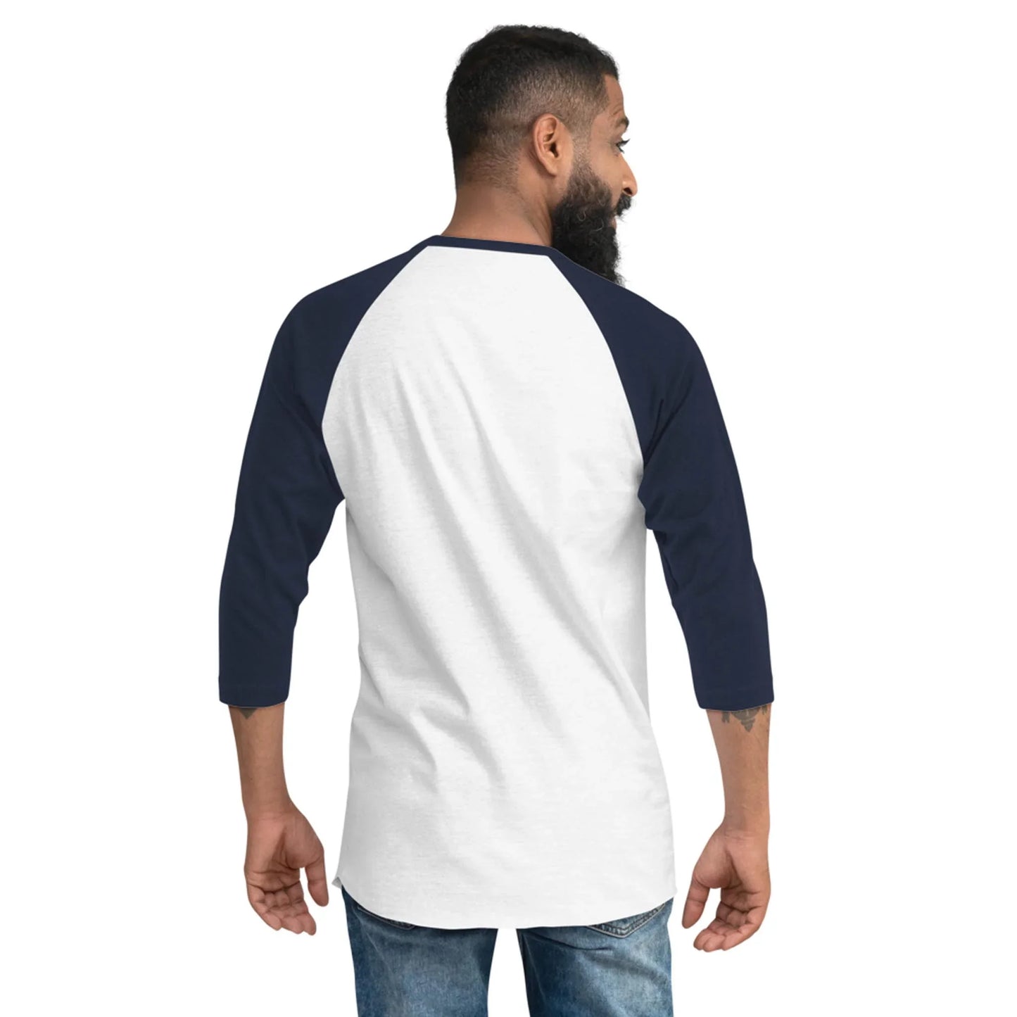 A man with a beard, wearing a white and navy Mambí raglan three-quarter sleeve shirt and jeans, stands facing away and slightly to the side against a plain background.