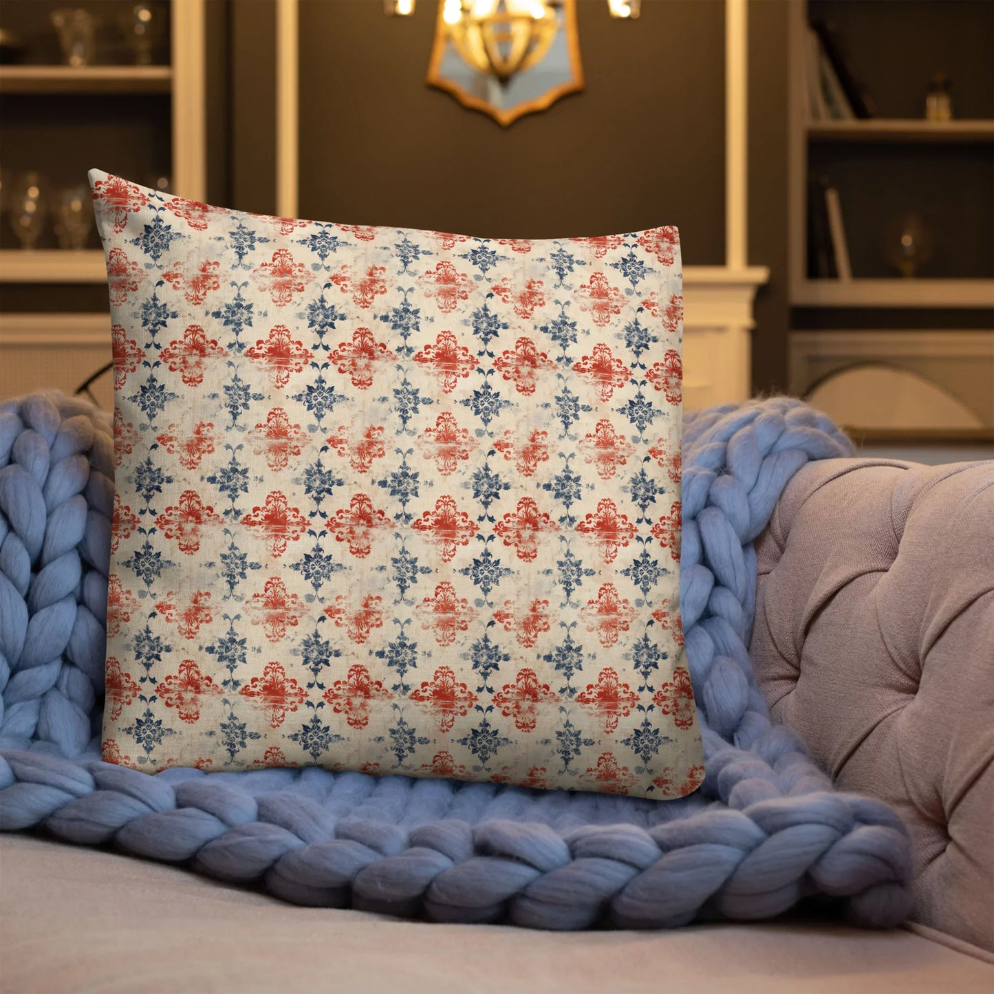 Red and blue decorative pillow on tufted sofa with chunky blue knit blanket in cozy living room.