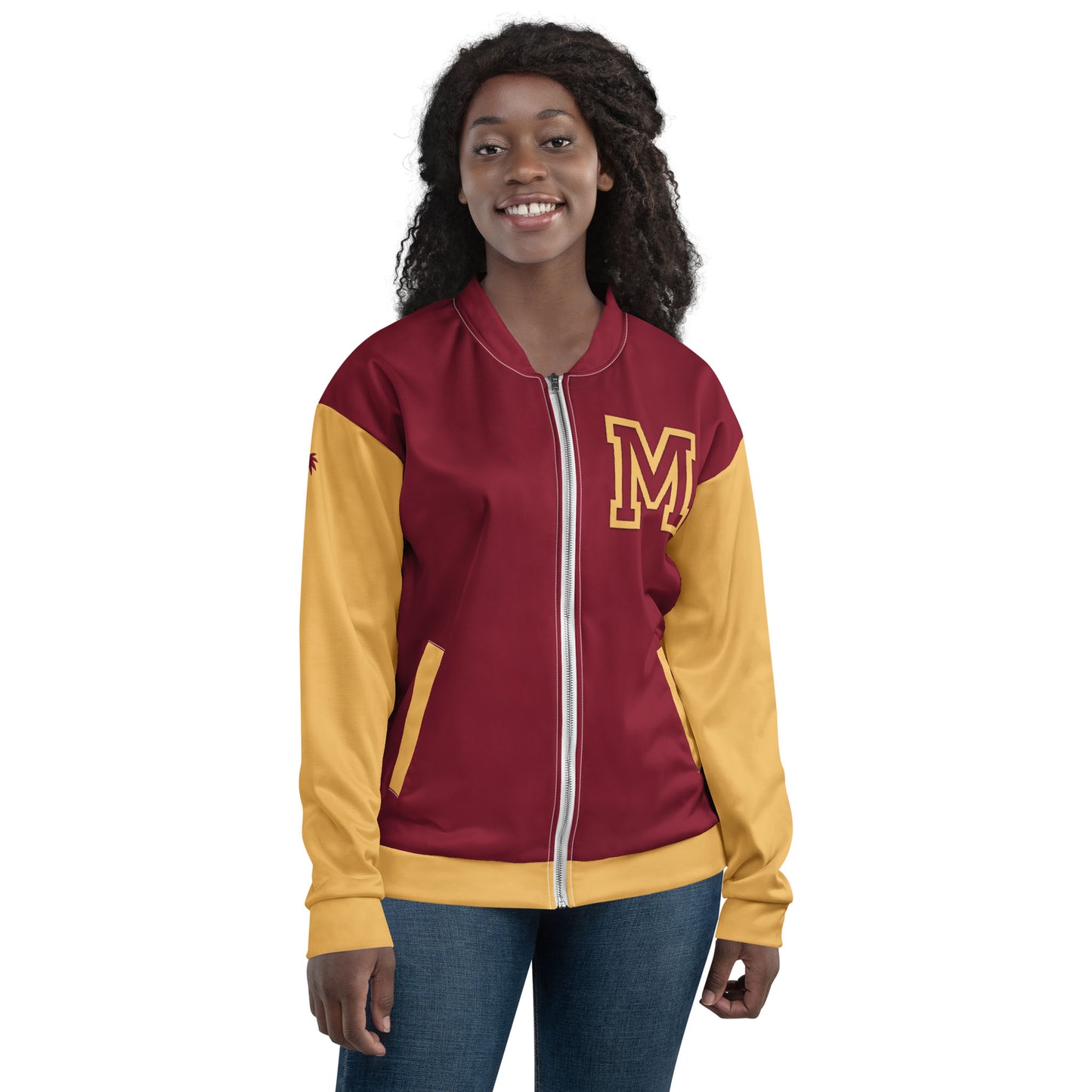 A woman smiling and wearing a maroon and yellow varsity bomber jacket with premium stitching and a large letter M on the left chest, standing with her hands relaxed at her sides.