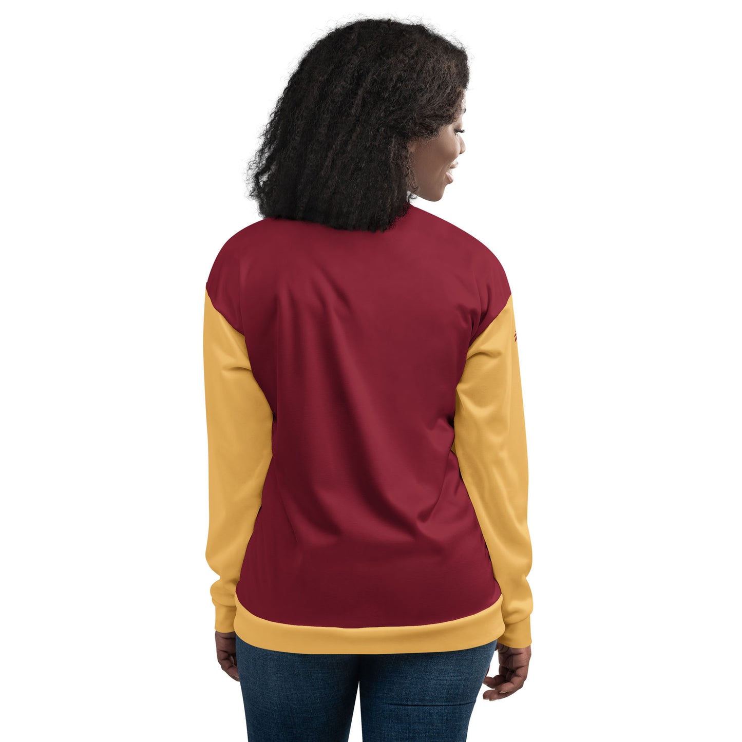 A woman with curly hair stands facing away, wearing a color-blocked varsity bomber jacket with maroon on the back, yellow sleeves and waistband, and premium stitching, paired with blue jeans.