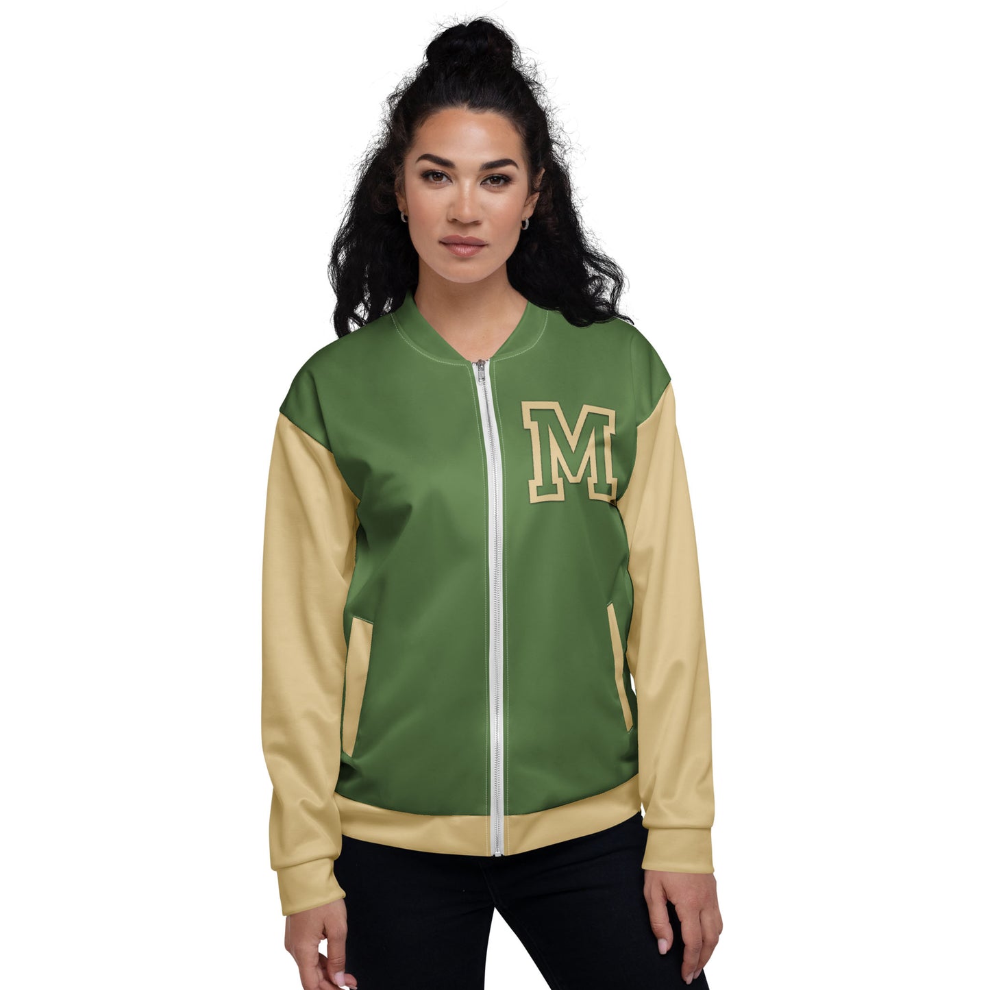 A woman with long, dark curly hair wears a green and beige varsity bomber jacket with premium stitching and a large letter M on the upper left chest. She stands facing forward with a neutral expression.