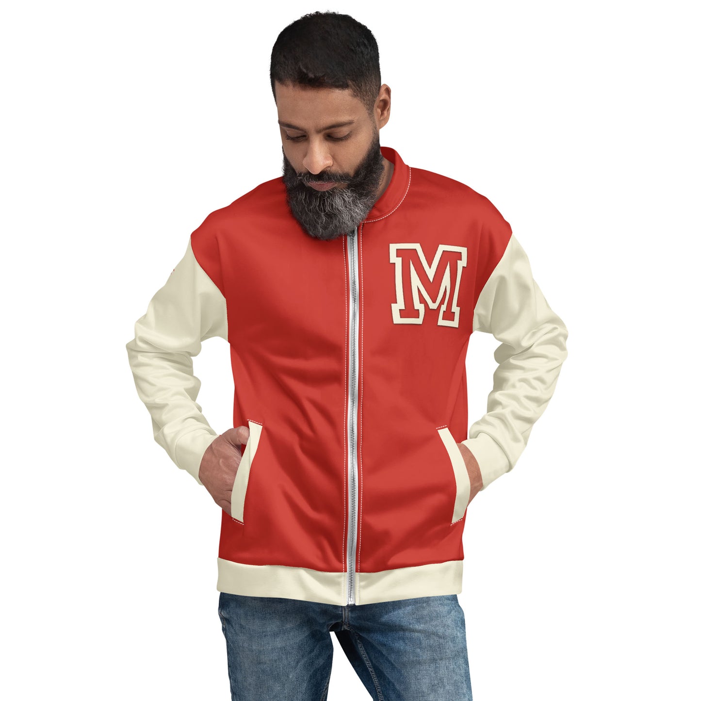 A man with a beard looks down with hands in the pockets of a red and white letterman jacket featuring premium stitching and a large letter M on the chest, paired with blue jeans.