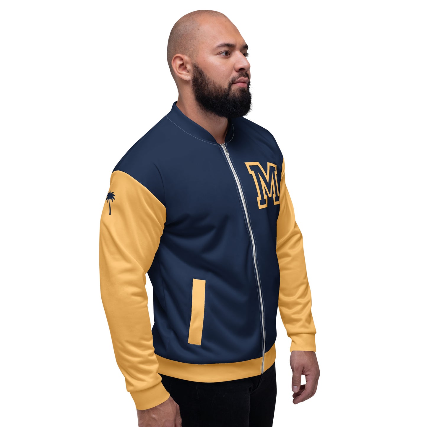 A man with a beard wears a navy and yellow varsity bomber jacket featuring premium stitching, a large M on the chest, and a small black palm tree on the sleeve, standing against a plain white background.