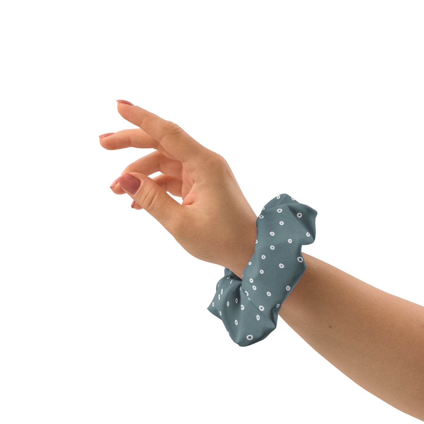 A hand with light skin is raised gracefully, wearing a blue recycled polyester scrunchie with white polka dots on the wrist, against a plain white background—an eco-friendly hair accessory.
