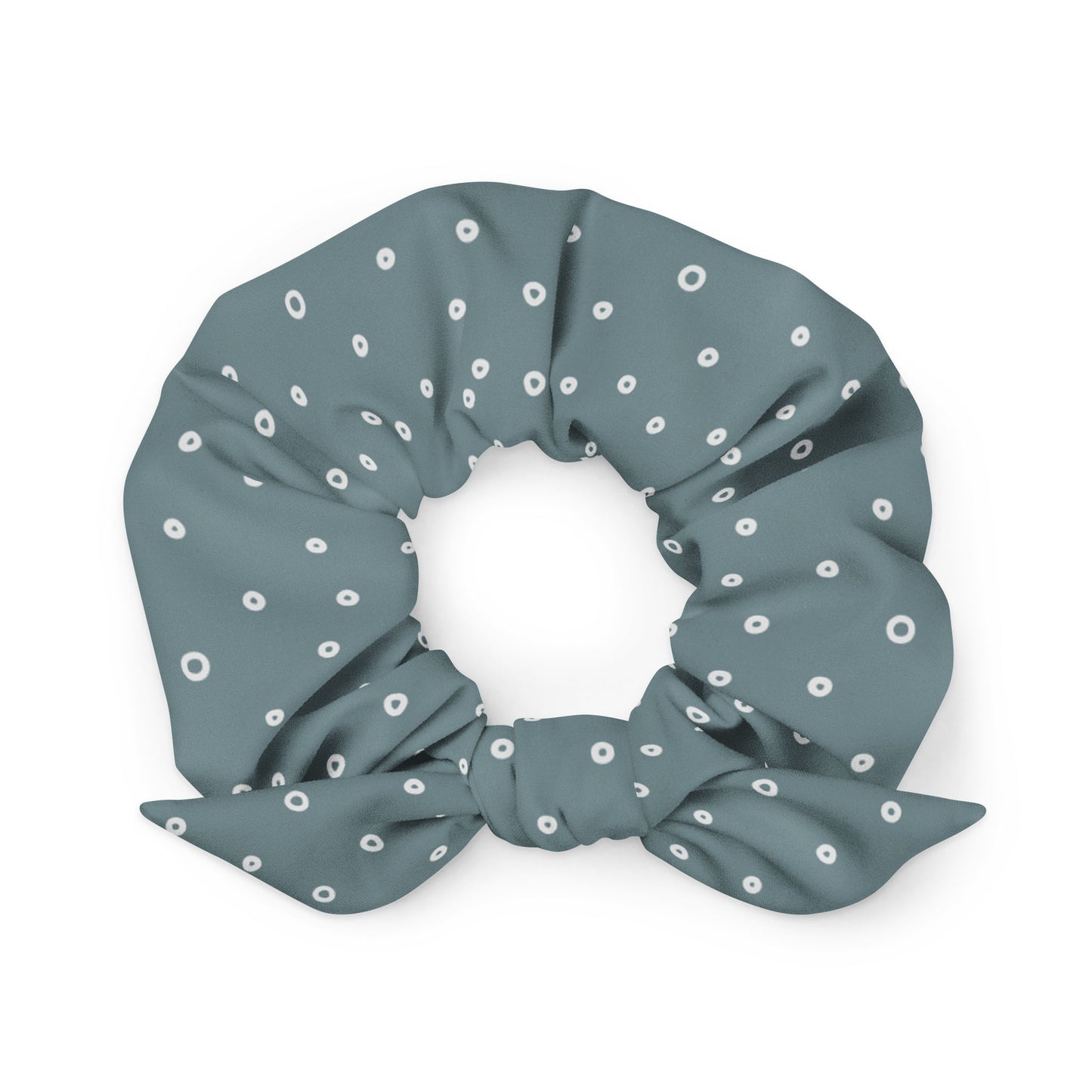 A teal recycled polyester scrunchie with white polka dots and a small bow attached, arranged in a circular shape against a white background.