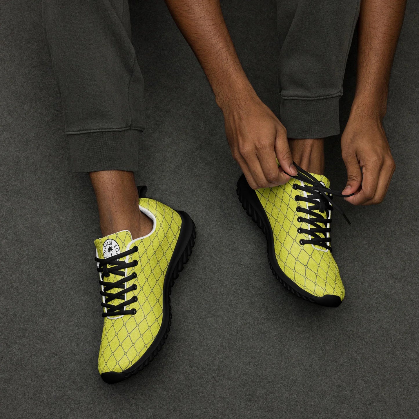 Man tying laces on yellow geometric athletic shoes with black soles on gray floor