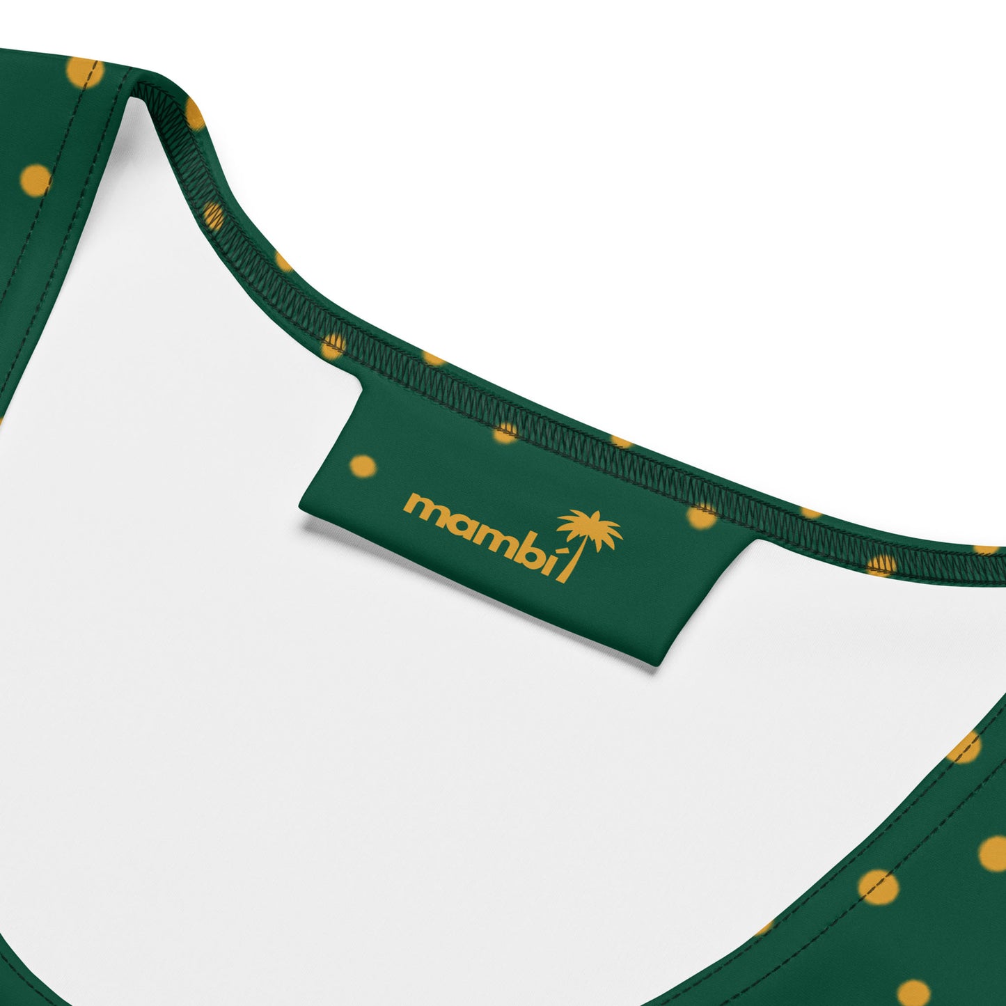 Close-up of a green microfiber yarn dress with yellow polka dots, focusing on the inside label that reads mambill with a palm tree icon. The inner lining is white.
