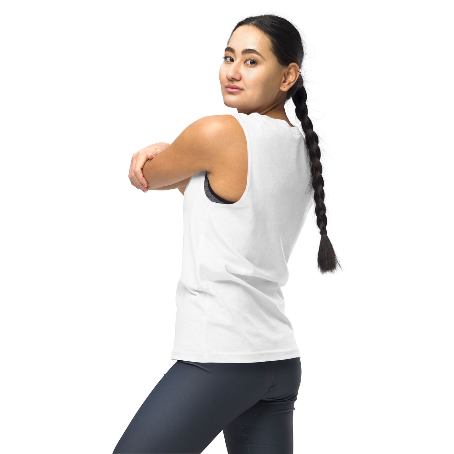 A woman with a long braid, wearing a white sleeveless tank and dark leggings, stands sideways against a white background, looking over her shoulder and stretching her arm across her chest as if ready for yoga class.